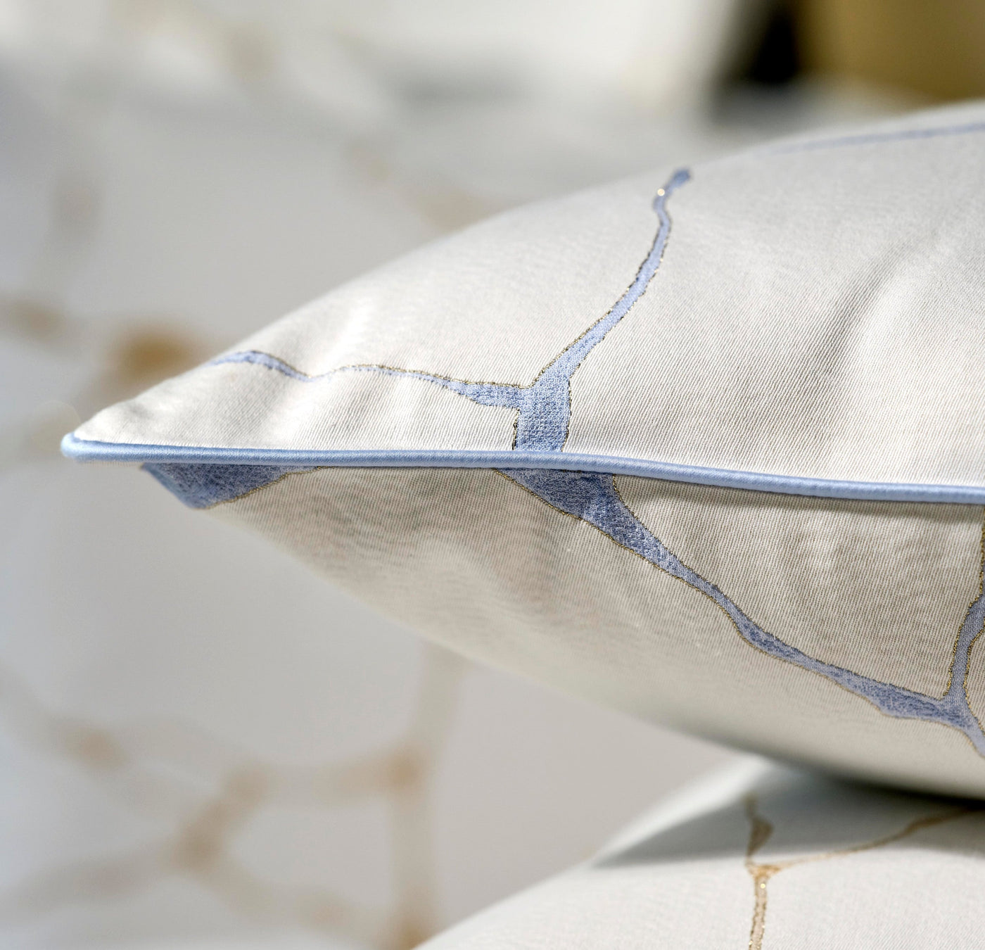 Close-up of a textured white pillowcase with blue embroidered accents and a subtle gold thread detail, featuring Jessie Pillowcase by Celso de Lemos available at Linen Society.