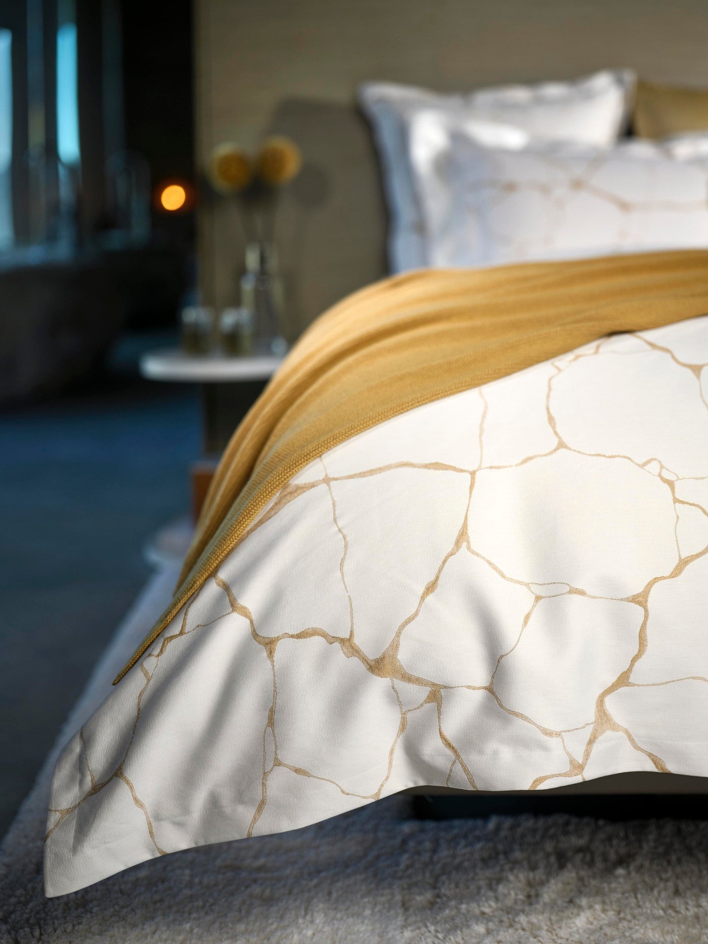 White pillowcase with a gold cracked pattern, accented by a golden throw, featuring Jessie Pillowcase by Celso de Lemos available at Linen Society.
