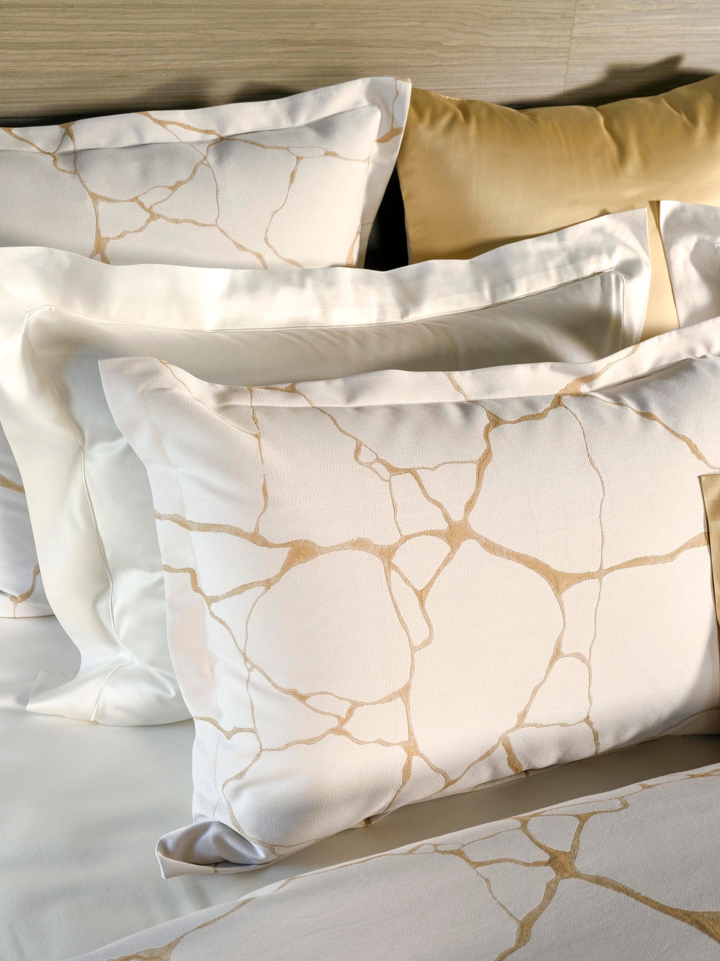 White pillowcase with a subtle gold abstract pattern, neatly stacked on a bed featuring Jessie Pillowcase by Celso de Lemos available at Linen Society.