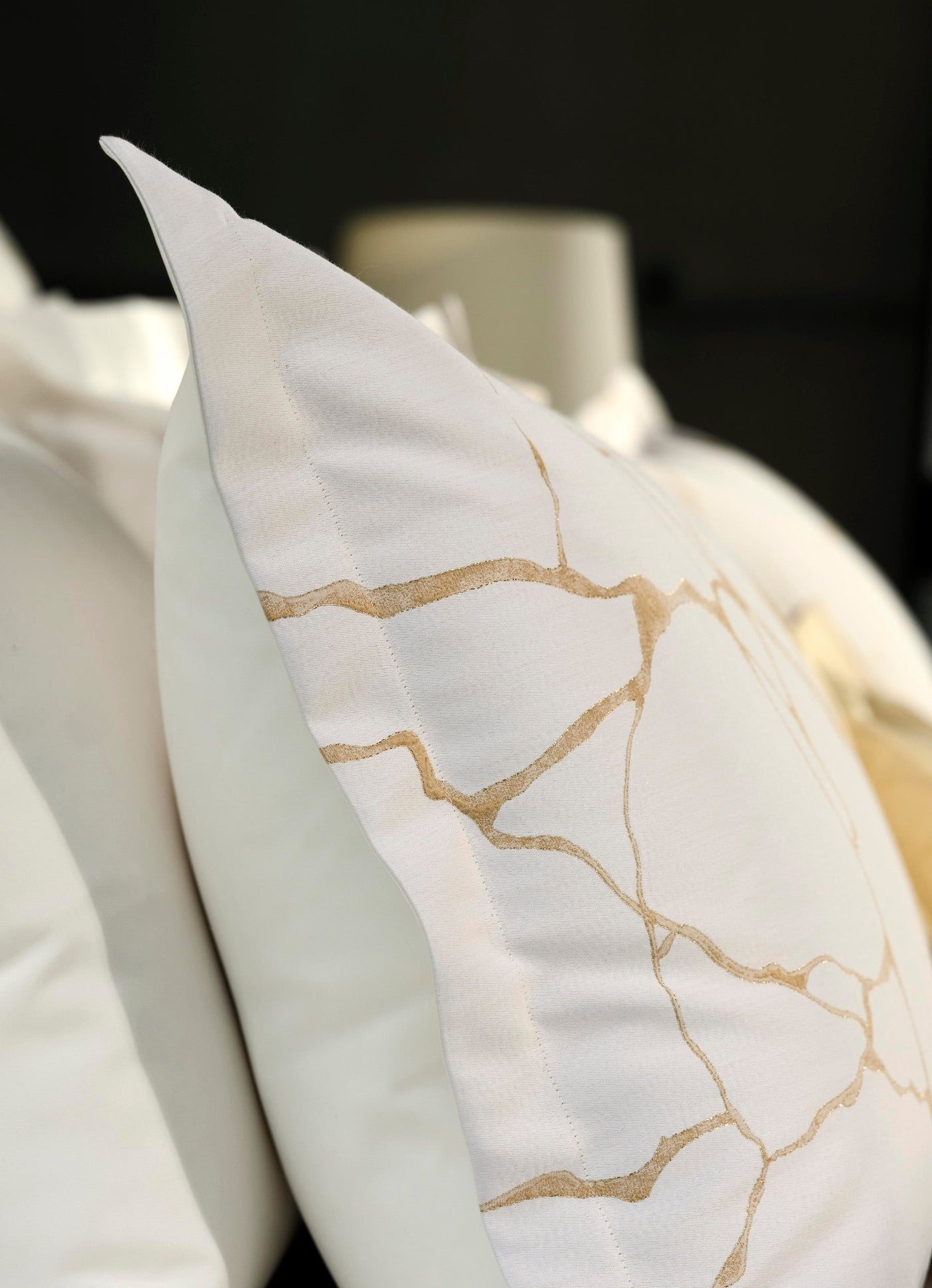 Close up of a white pillow with a subtle gold abstract pattern, featuring Jessie Pillowcase by Celso de Lemos available at Linen Society.