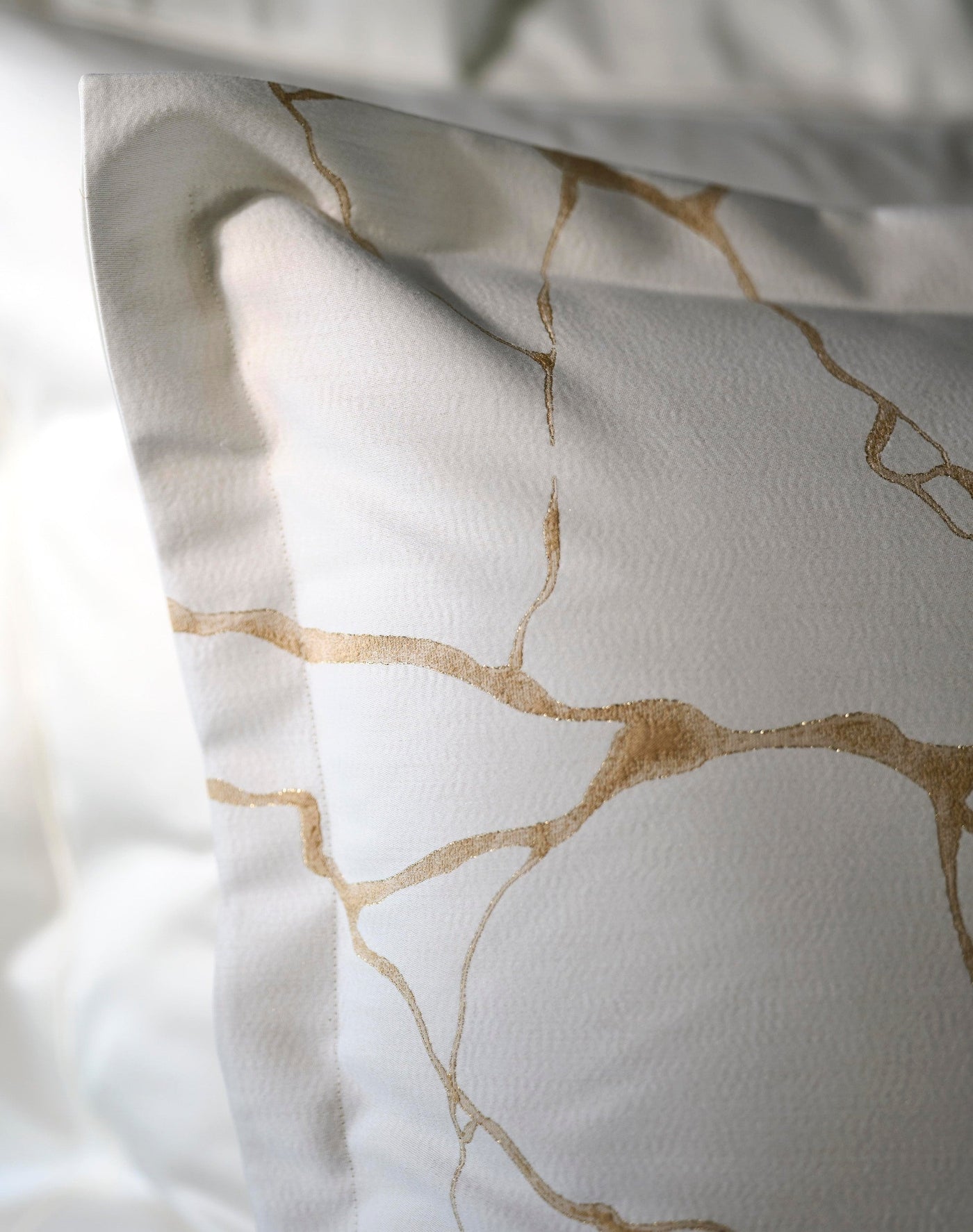 Close-up of a white pillowcase with a subtle texture and scattered gold abstract lines, featuring Jessie Pillowcase by Celso de Lemos available at Linen Society.