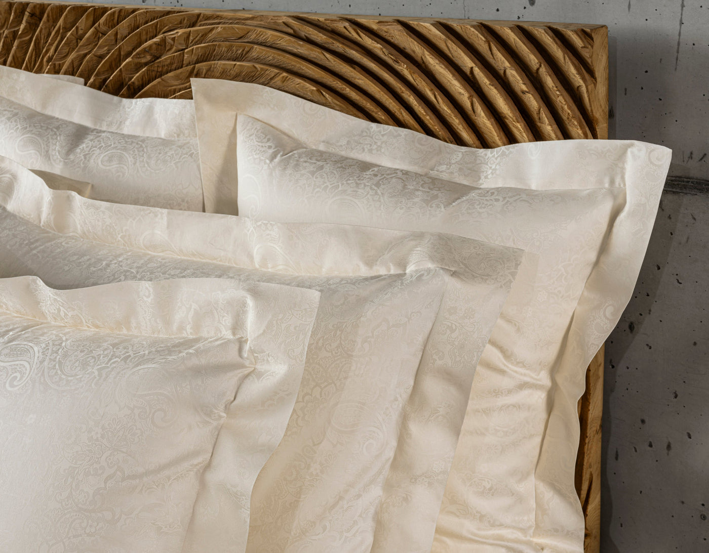 Cream woven Pillowcase with a subtle paisley pattern neatly folded on a wooden headboard, featuring Joanne Pillowcase by Celso de Lemos available at Linen Society.