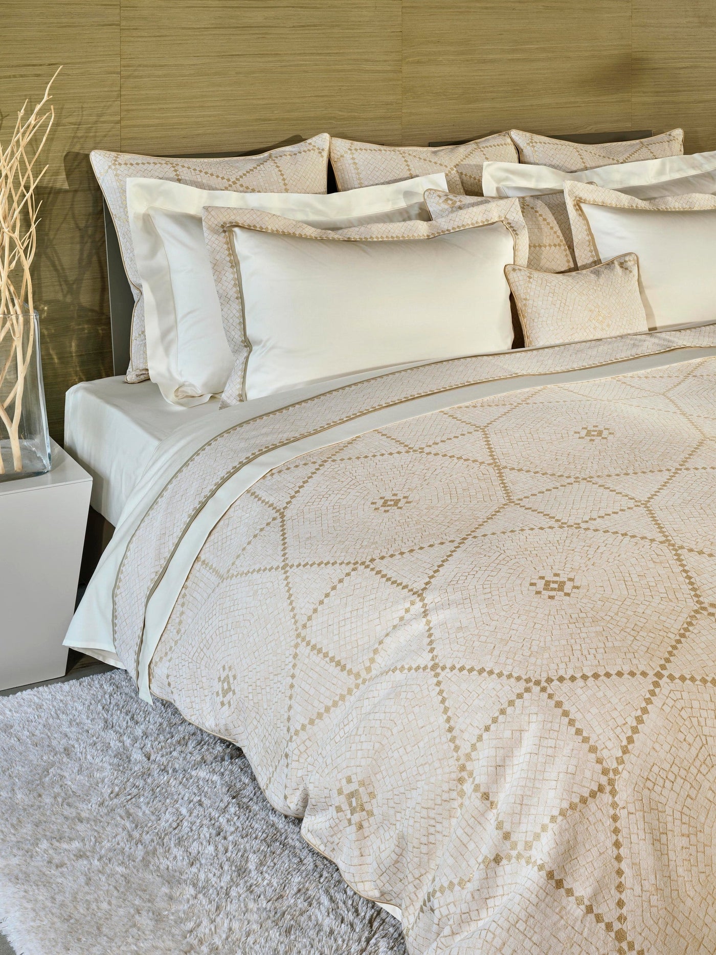 A neatly made bed with white linens and a duvet featuring a subtle geometric pattern in beige and gold. featuring Kerylos Pillowcase by Celso de Lemos available at Linen Society.