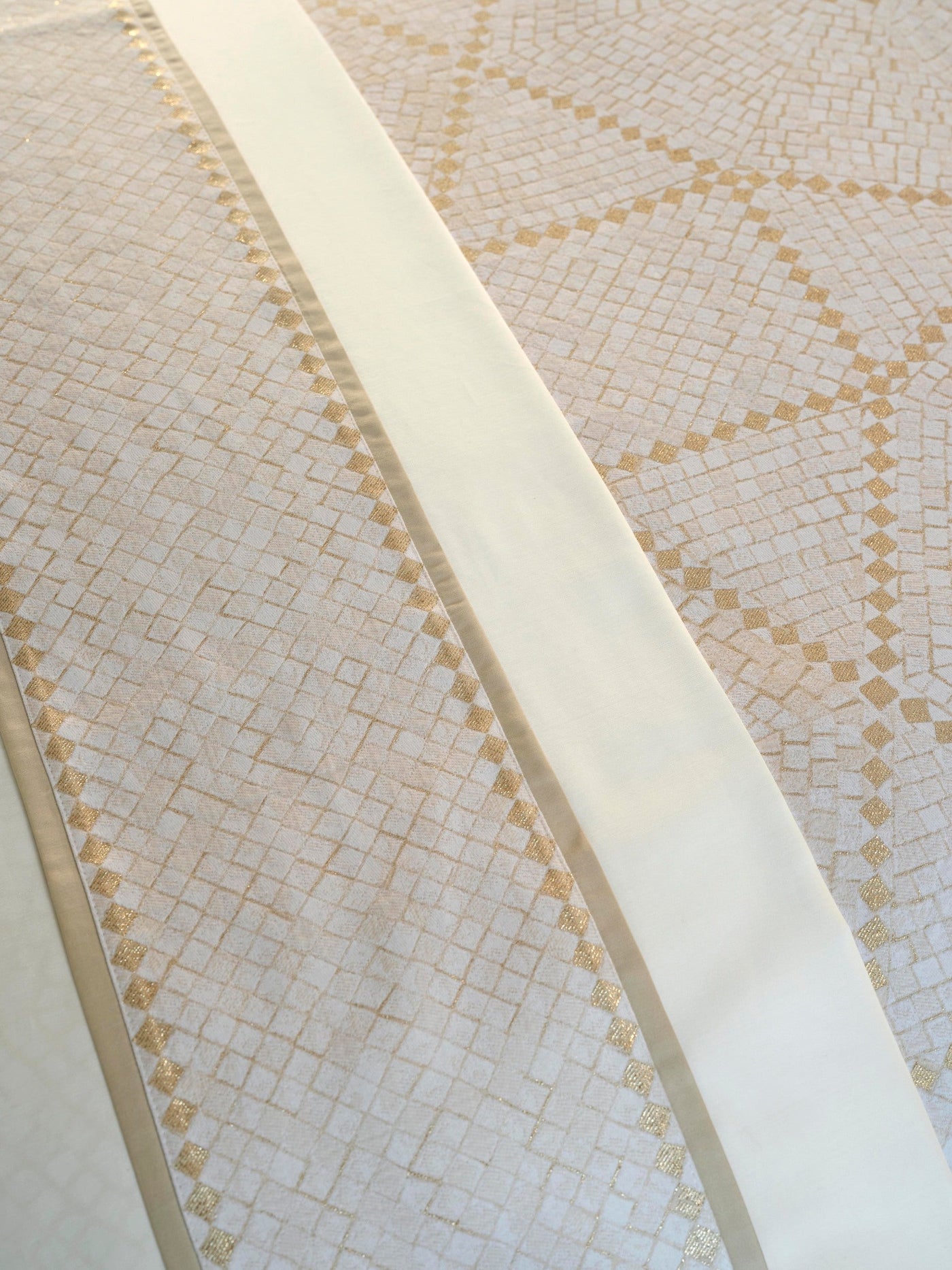Close-up of a textured cream fabric with a subtle gold mosaic pattern and a solid cream band, featuring Kerylos Pillowcase by Celso de Lemos available at Linen Society.