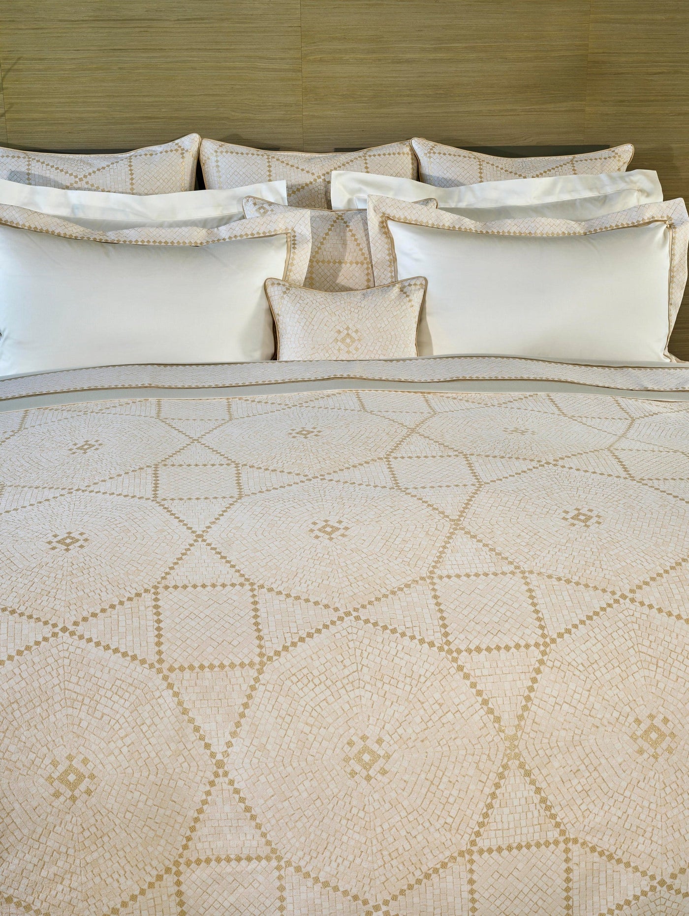 Plush white pillows and a quilt with a geometric mosaic pattern are displayed on a bed. featuring Kerylos Pillowcase by Celso de Lemos available at Linen Society.
