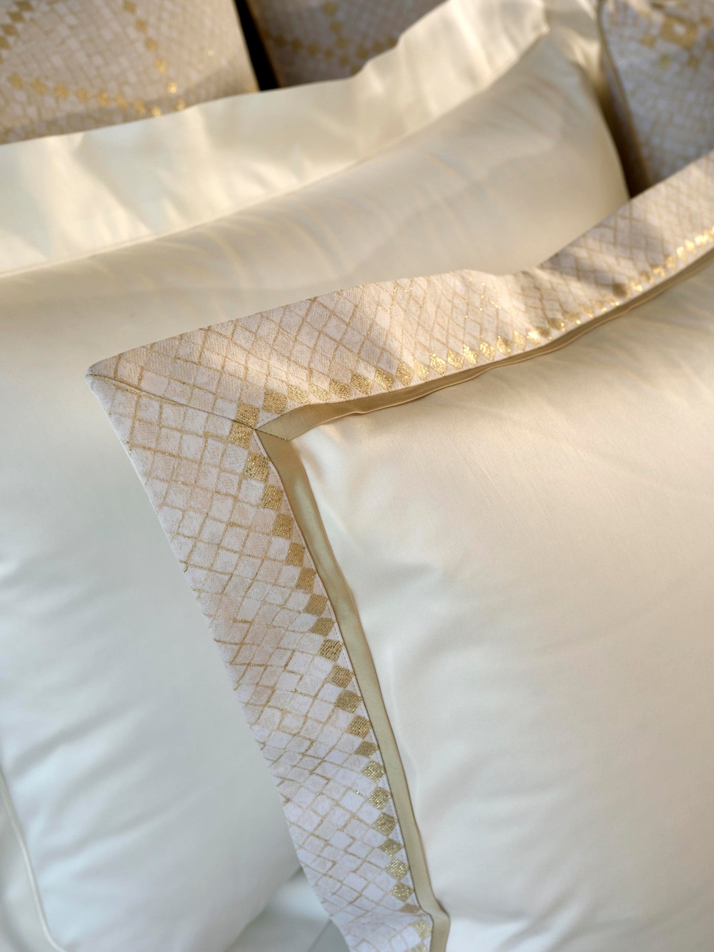 Close-up of cream pillows with a textured gold diamond border, featuring Kerylos Pillowcase by Celso de Lemos available at Linen Society.