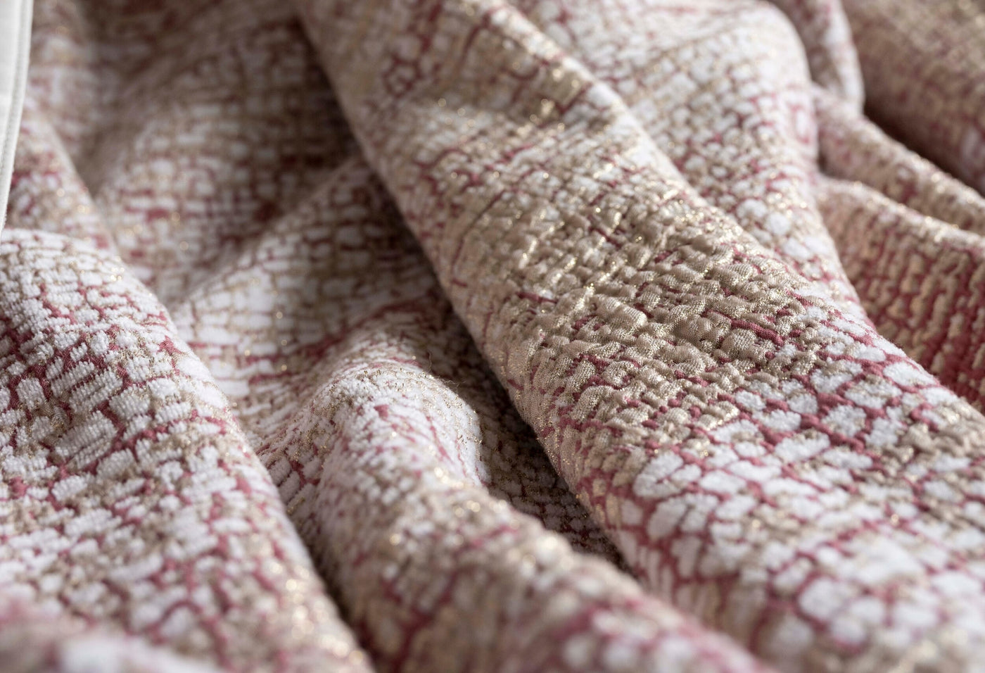 Close-up view of a textured, woven fabric with a pattern of pink and gold threads on a white background, featuring Lems Bed Cover by Celso de Lemos available at Linen Society.