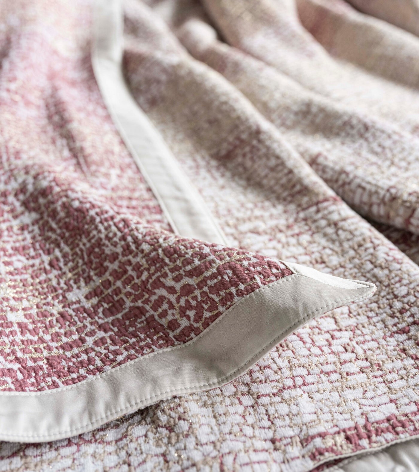 Close-up view of a textured, woven bed cover in white, rose, and gold with a neutral trim, featuring Lems Bed Cover by Celso de Lemos available at Linen Society.