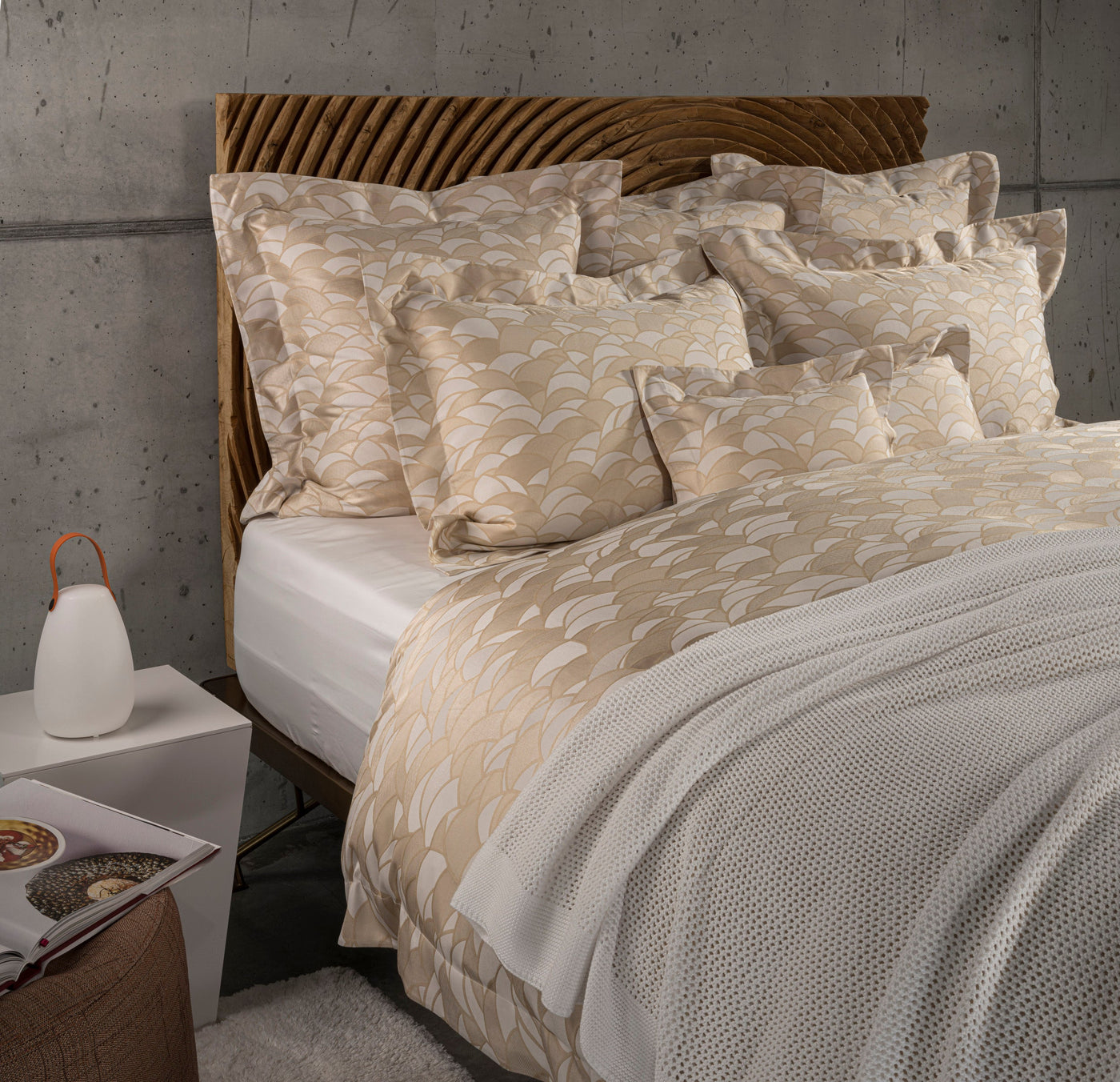 A bed features a headboard and a duvet with a cream and gold geometric pattern, a white throw blanket, and a white accent pillow, featuring Loulou Pillowcase by Celso de Lemos available at Linen Society.