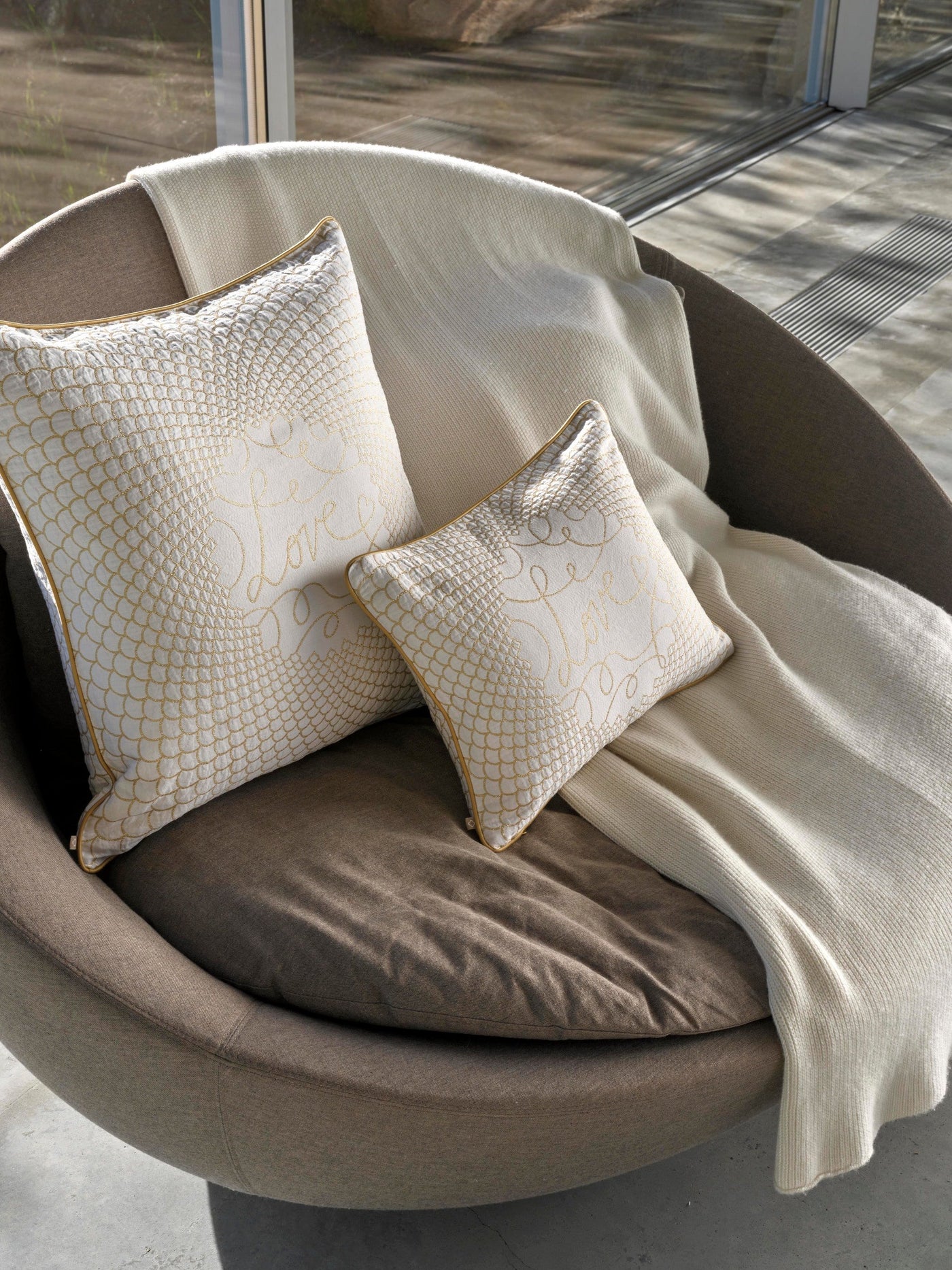 Two white pillow covers with gold intricate embroidery rest on a chair, featuring the Love Pillow Cover by Celso de Lemos available at Linen Society.