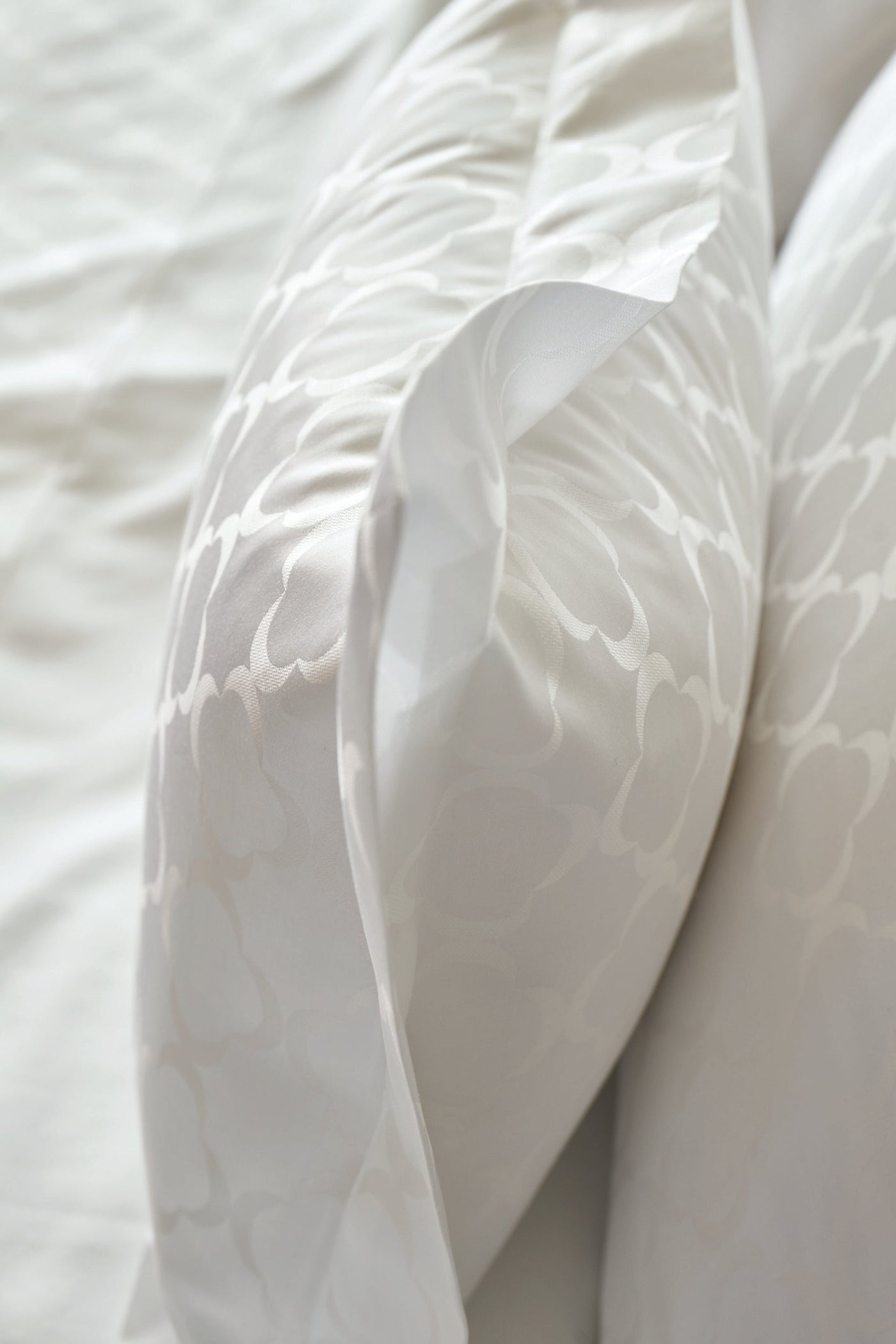 Close-up of white bedding with a subtle, tonal damask pattern on a pillowcase, featuring Lua Pillowcase by Celso de Lemos available at Linen Society.