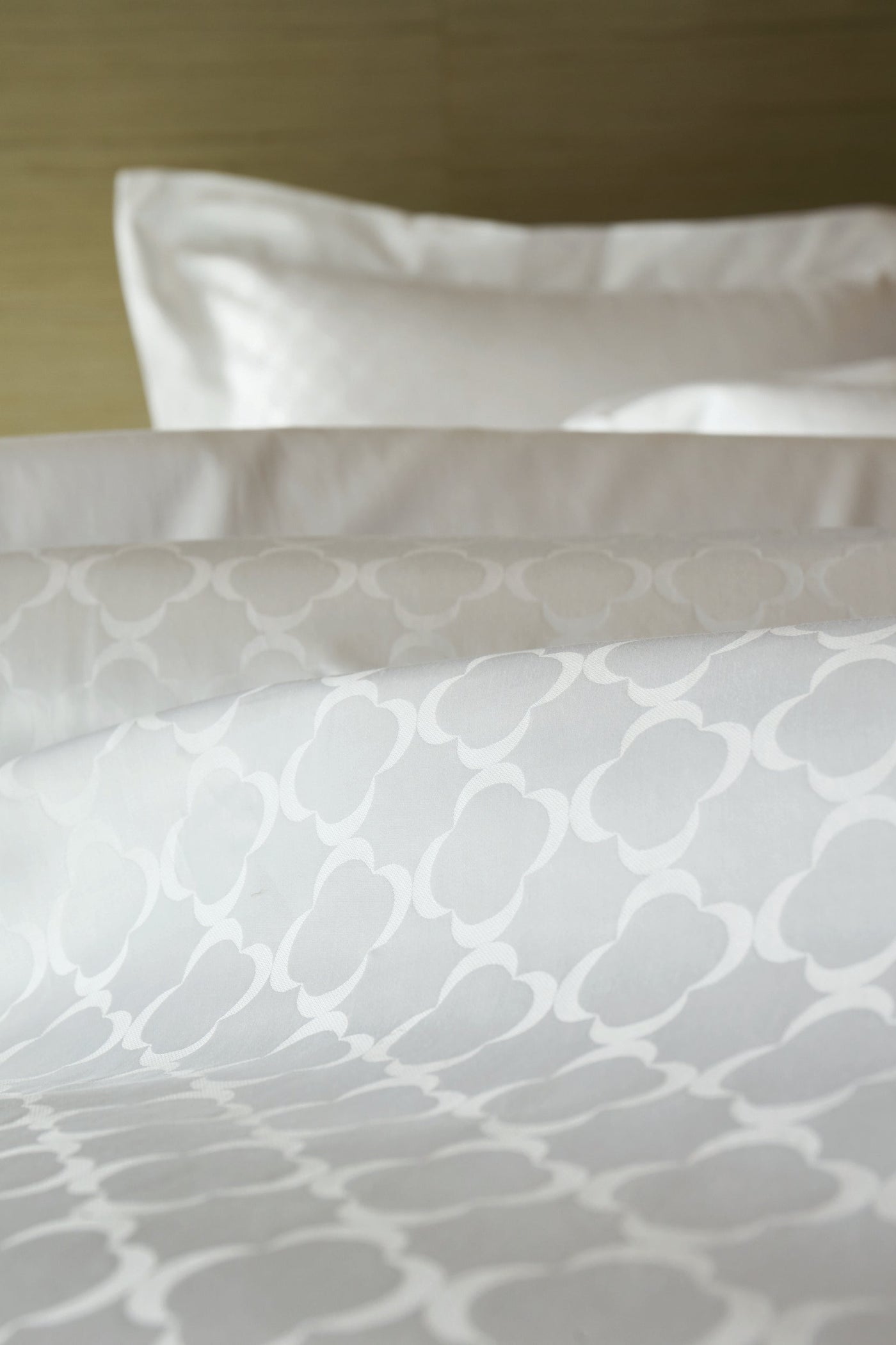 Close-up of white patterned bedding with a subtle geometric design, featuring Lua Pillowcase by Celso de Lemos available at Linen Society.