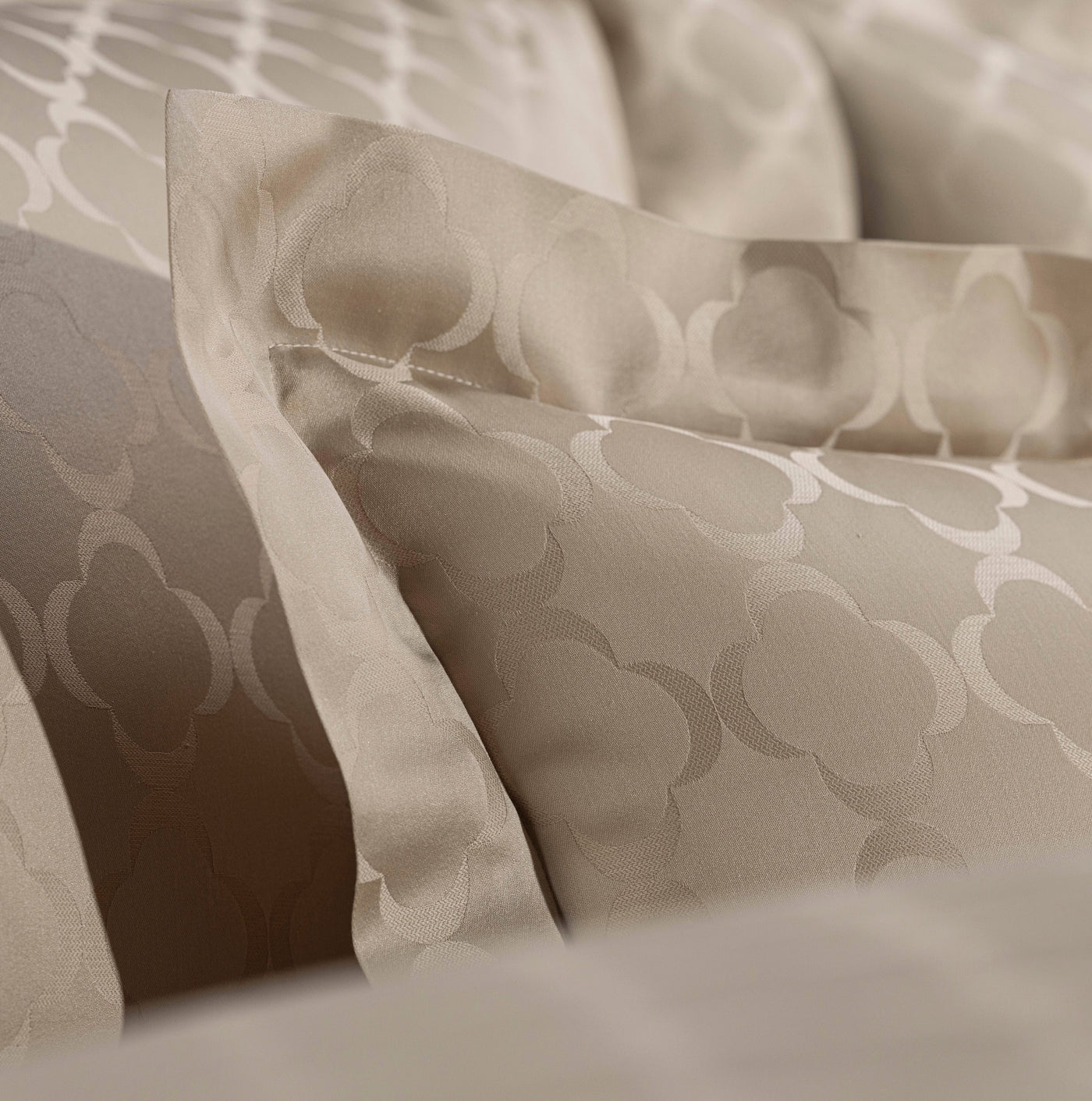 Close-up of folded beige pillowcases with a subtle woven geometric pattern, featuring Lua Pillowcase by Celso de Lemos available at Linen Society.