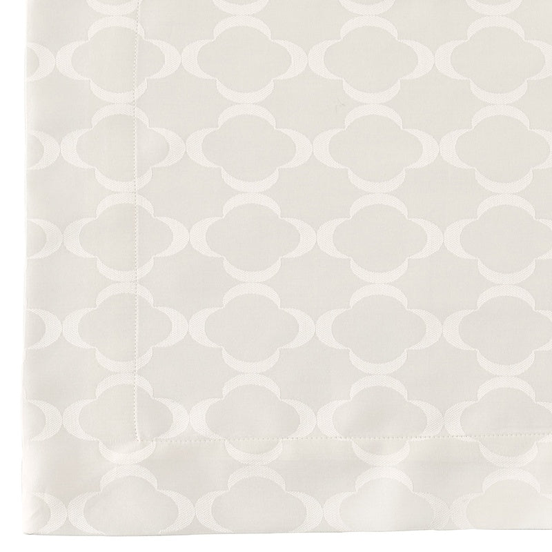 A close-up of a light cream fabric with a subtle tone-on-tone quatrefoil pattern and a stitched border, featuring Lua Pillowcase by Celso de Lemos available at Linen Society.