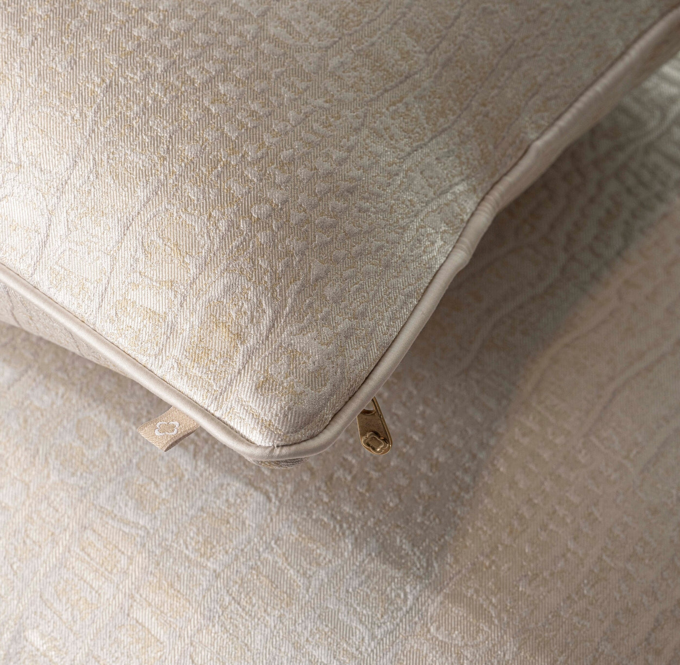 Close-up of a beige pillow cover with a subtle woven pattern and a gold zipper, featuring Luxe Pillow Cover by Celso de Lemos available at Linen Society.