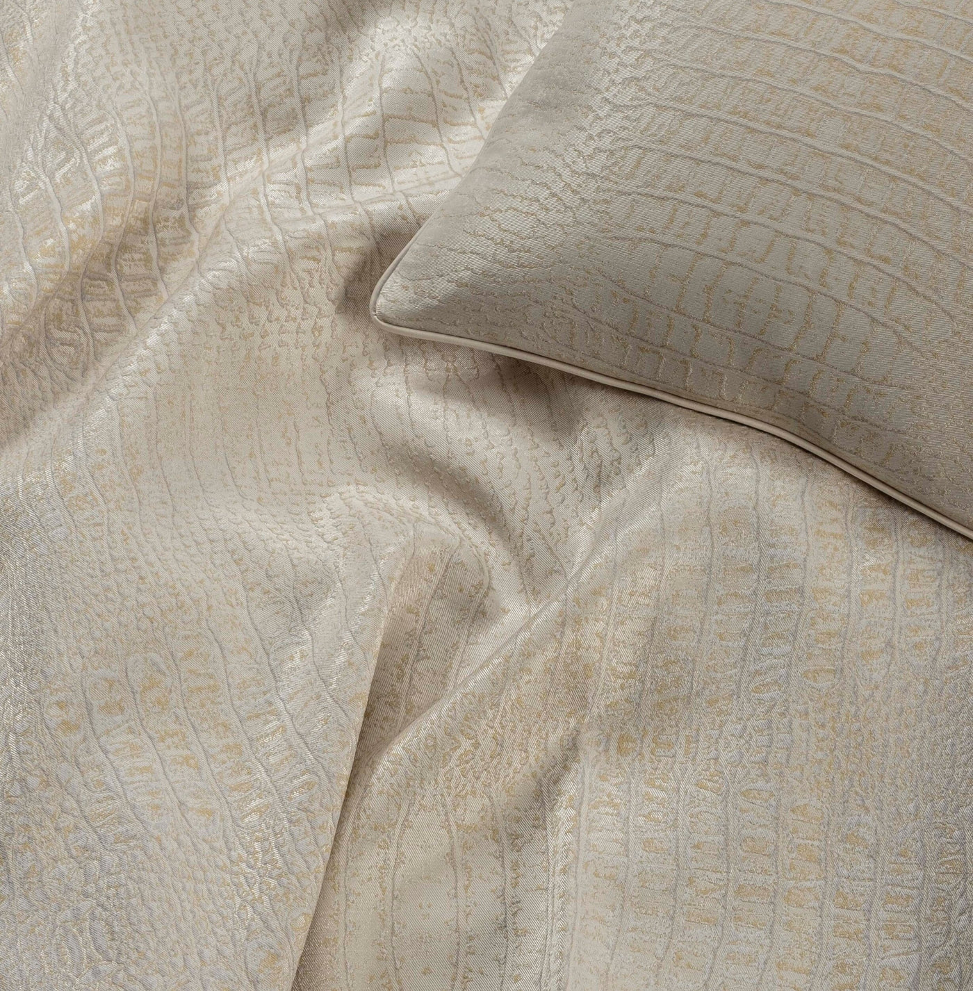 A pillow and draped fabric showcase a textured, crocodile-embossed pattern in a neutral, light tone, featuring Luxe Pillow Cover by Celso de Lemos available at Linen Society.