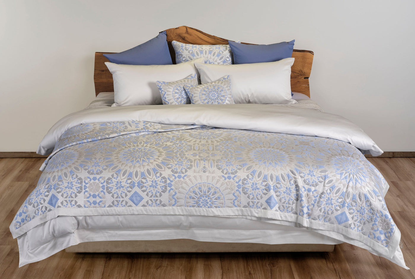A bed with white sheets and a duvet featuring a blue and silver geometric pattern. Two blue pillows and two white pillows are arranged at the head of the bed. featuring Milena Pillow Cover by Celso de Lemos available at Linen Society.