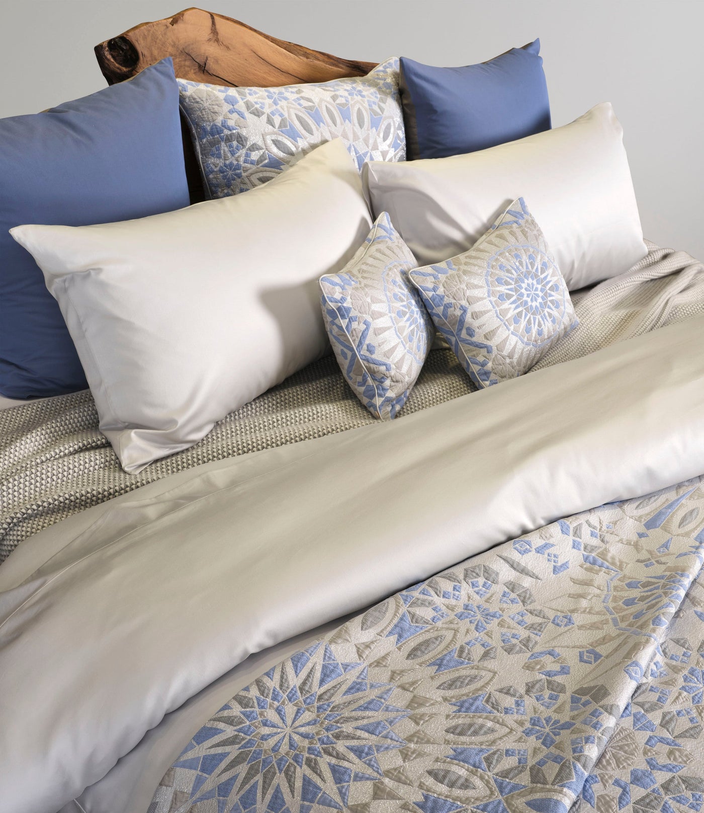 White and blue patterned accent pillows on a bed with a natural wood headboard, featuring Milena Accent Pillow by Celso de Lemos available at Linen Society.