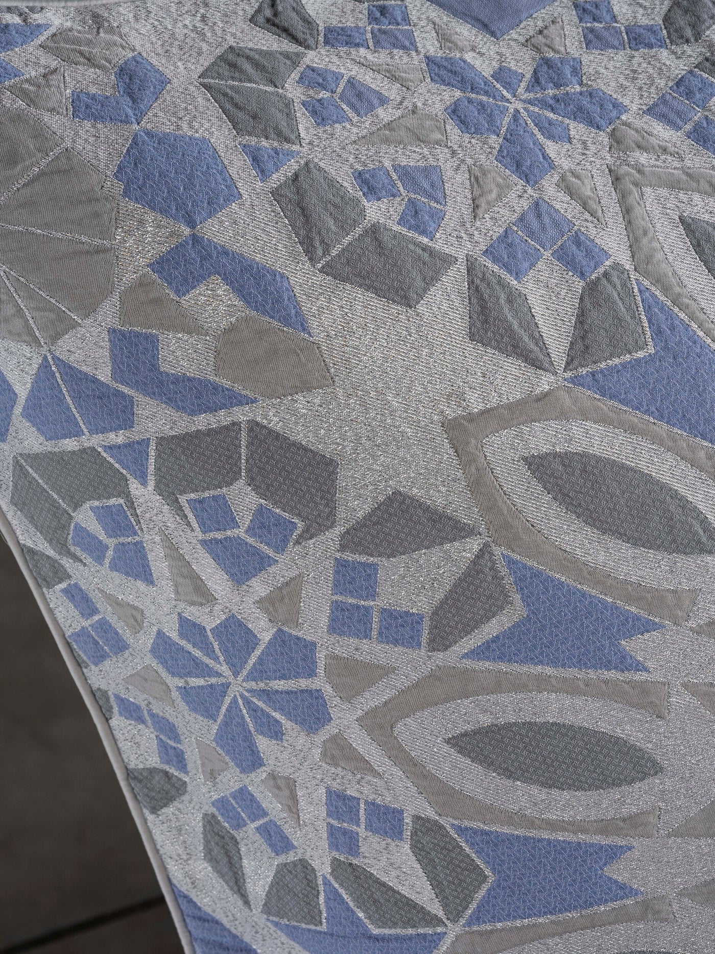 A textured fabric with a geometric pattern in shades of blue, grey, and silver, featuring Milena Cushion Cover by Celso de Lemos available at Linen Society.
