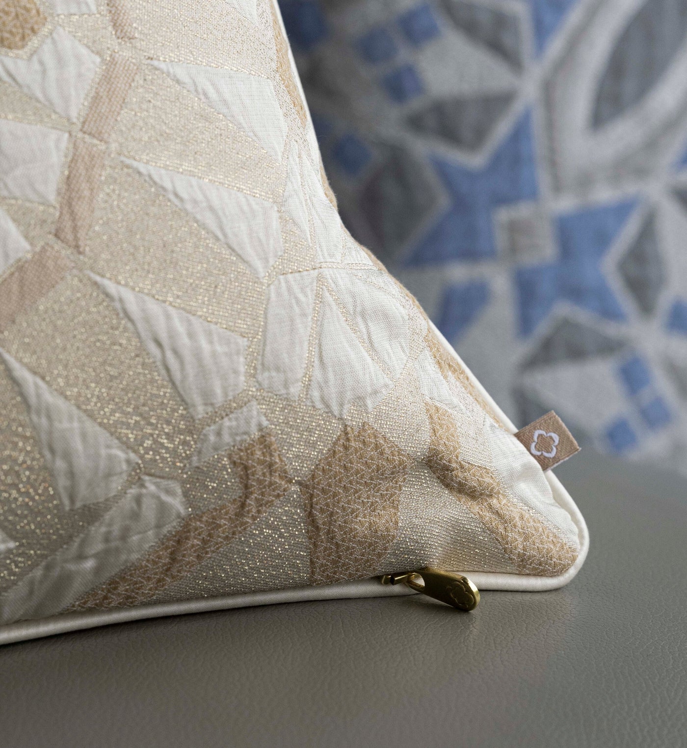 A cream pillow with a geometric gold pattern rests on a grey surface, featuring the Milena Pillow Cover by Celso de Lemos available at Linen Society.