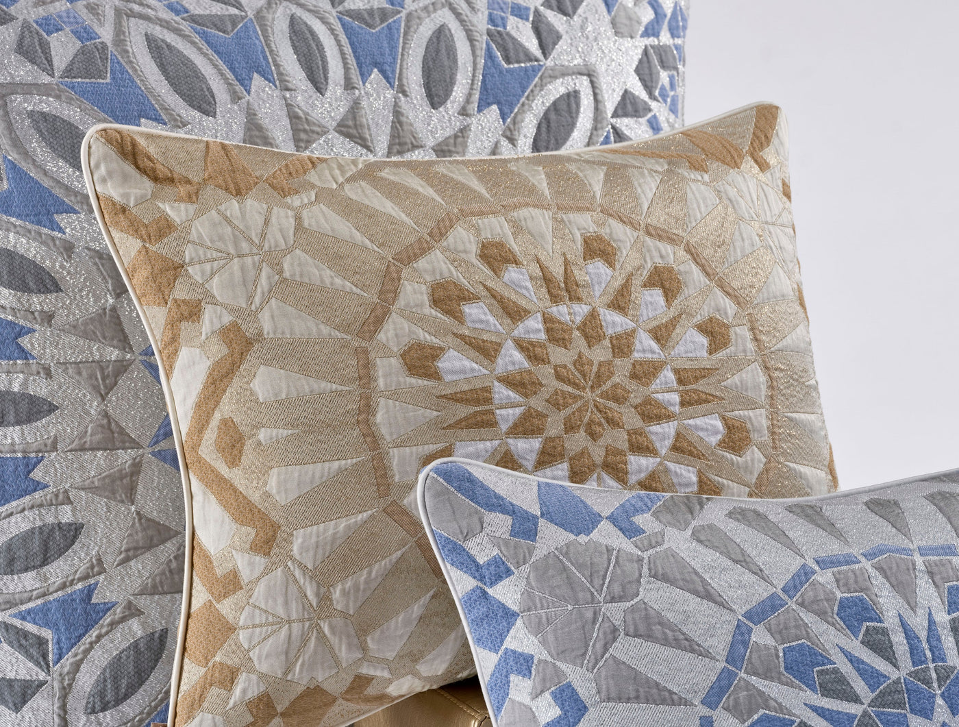 Three decorative pillows with geometric patterns in beige, gold, blue, and silver, featuring Milena Cushion Cover by Celso de Lemos available at Linen Society.