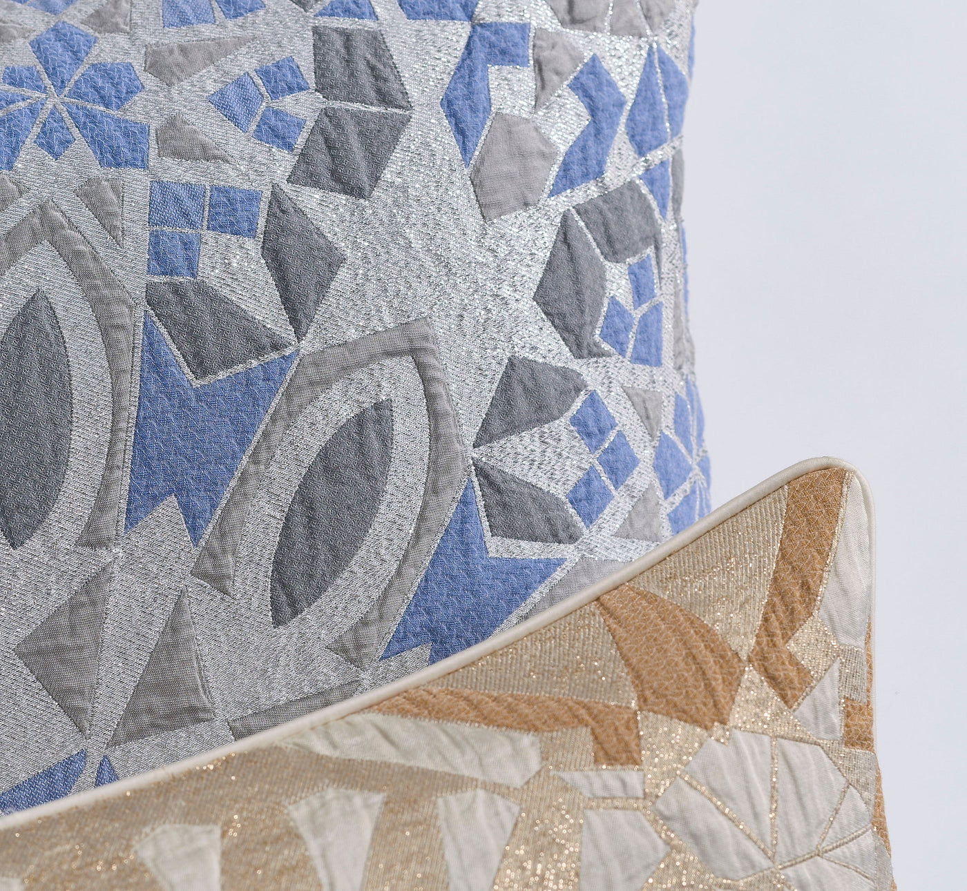 Two quilted pillow covers with geometric patterns in silver, blue, and gold featuring Milena Pillow Cover by Celso de Lemos available at Linen Society.