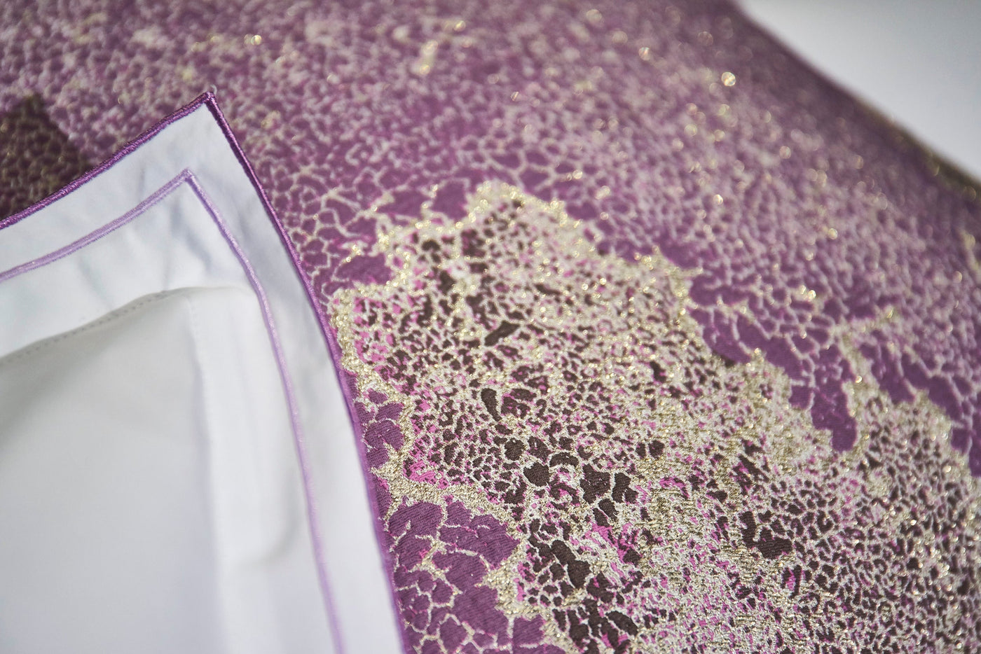 Close-up of a white pillow cover with a textured, patterned purple fabric featuring metallic gold accents, featuring Mundo Pillow Cover by Celso de Lemos available at Linen Society.