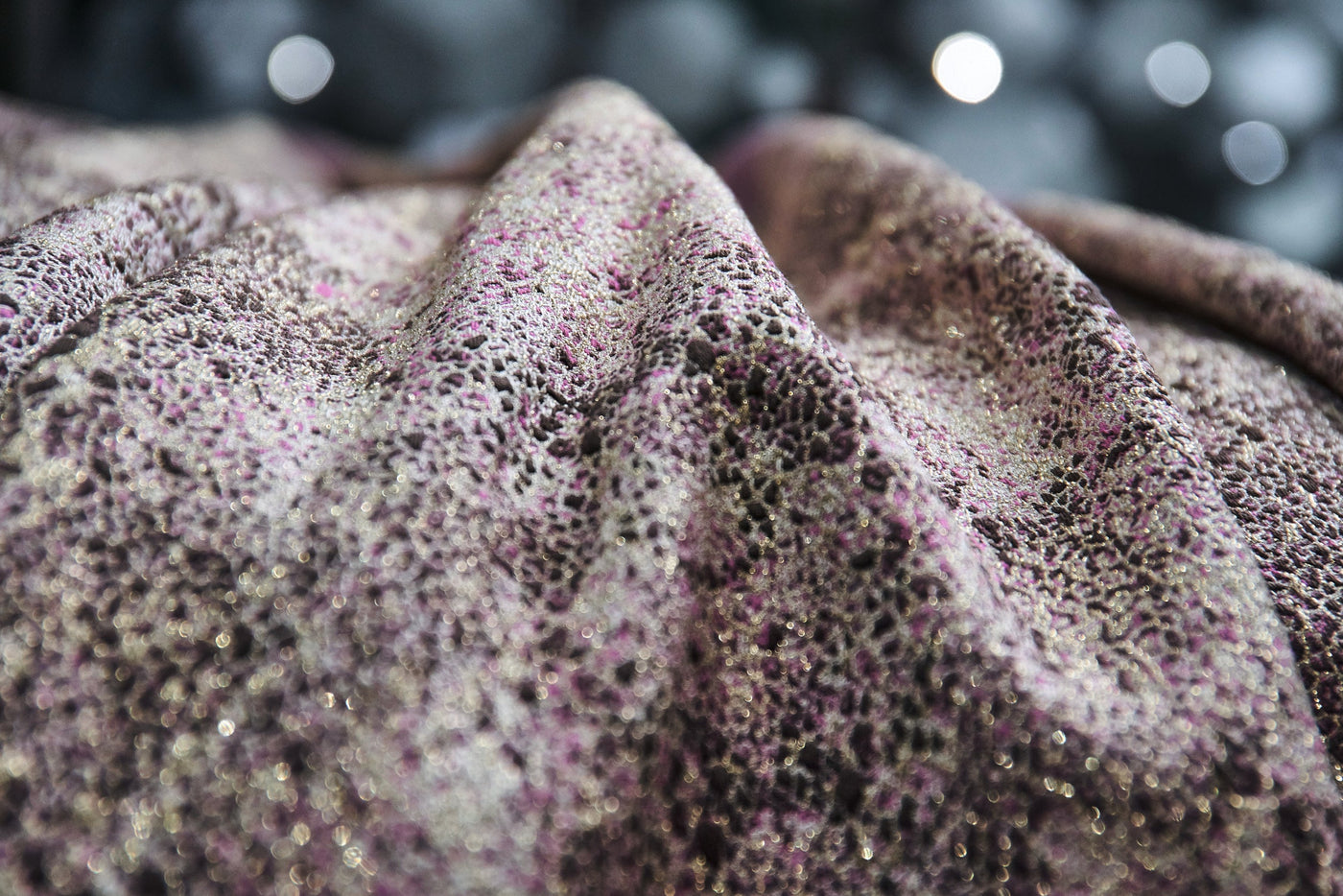 Close-up view of a textured fabric with a lace-like pattern in shades of purple and silver sparkle, featuring the Mundo Pillow Cover by Celso de Lemos available at Linen Society.
