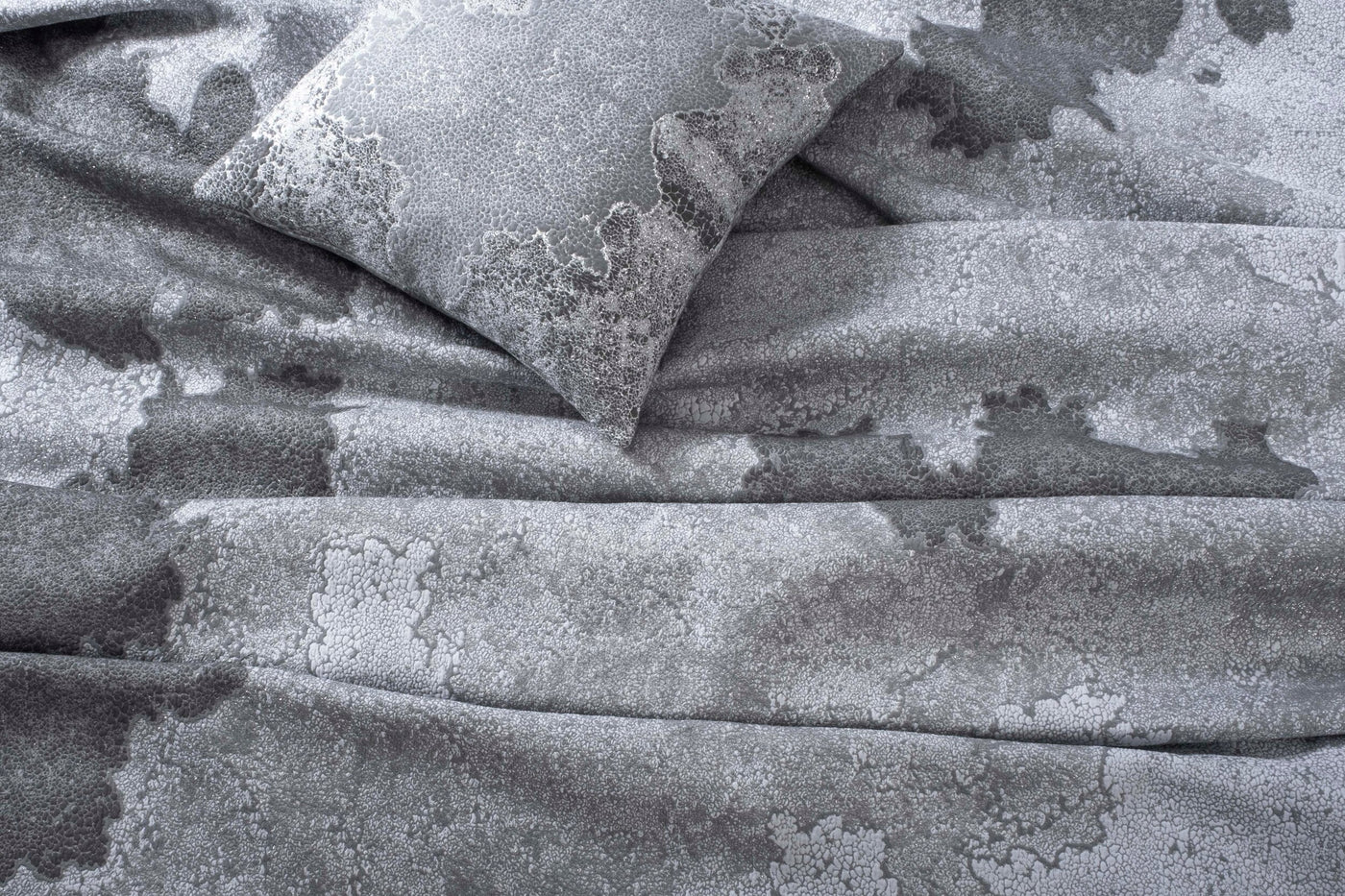 Close-up of a grey pillow with a textured, abstract pattern and draped fabric, featuring Mundo Pillow Cover by Celso de Lemos available at Linen Society.