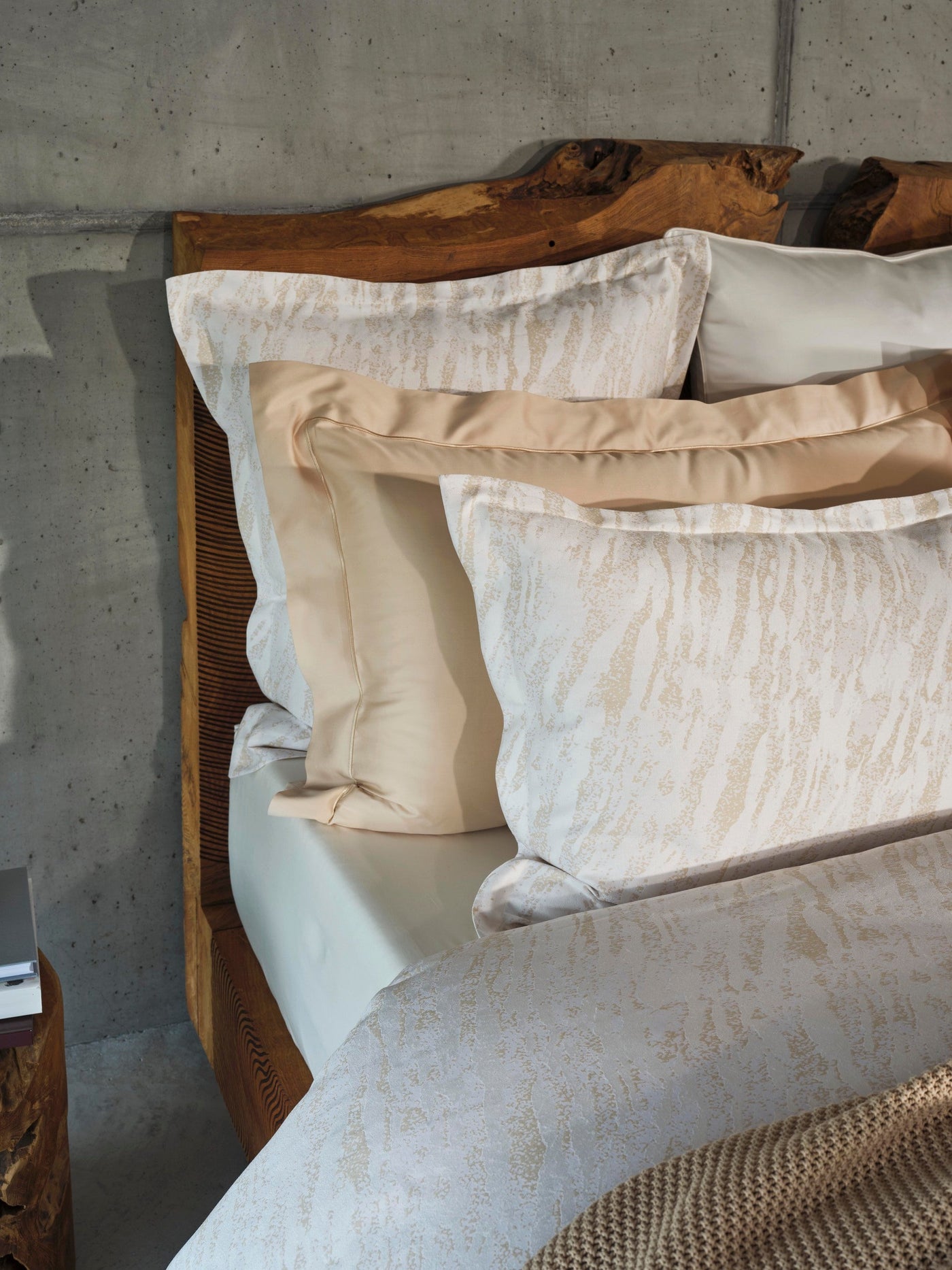 Close-up of Neve pillowcases in ivory with champagne jacquard pattern against rustic wood headboard.