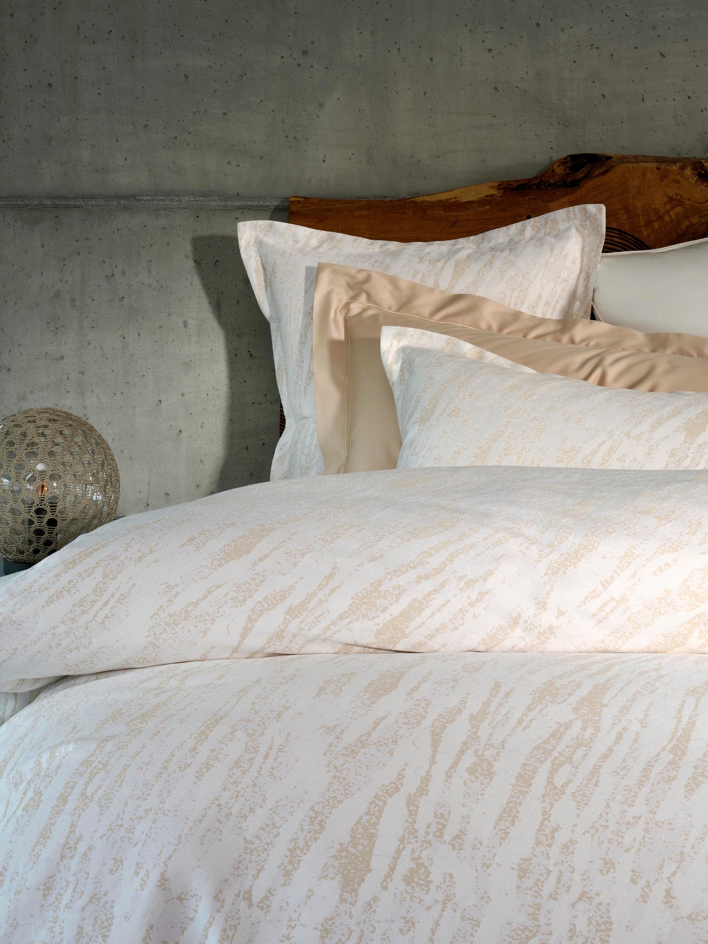 Close-up of Neve pillowcases in ivory with champagne wave-pattern texture against layered bedding.