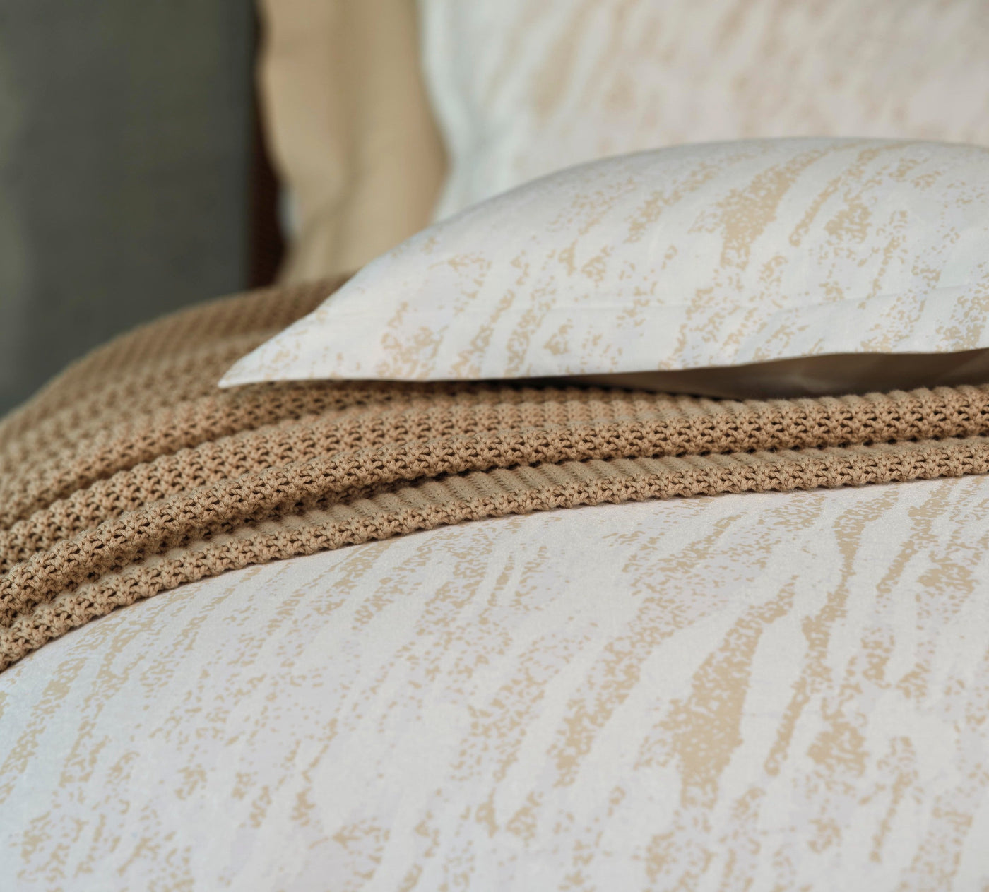 Close-up of ivory pillowcase with champagne abstract texture pattern atop matching bedding.