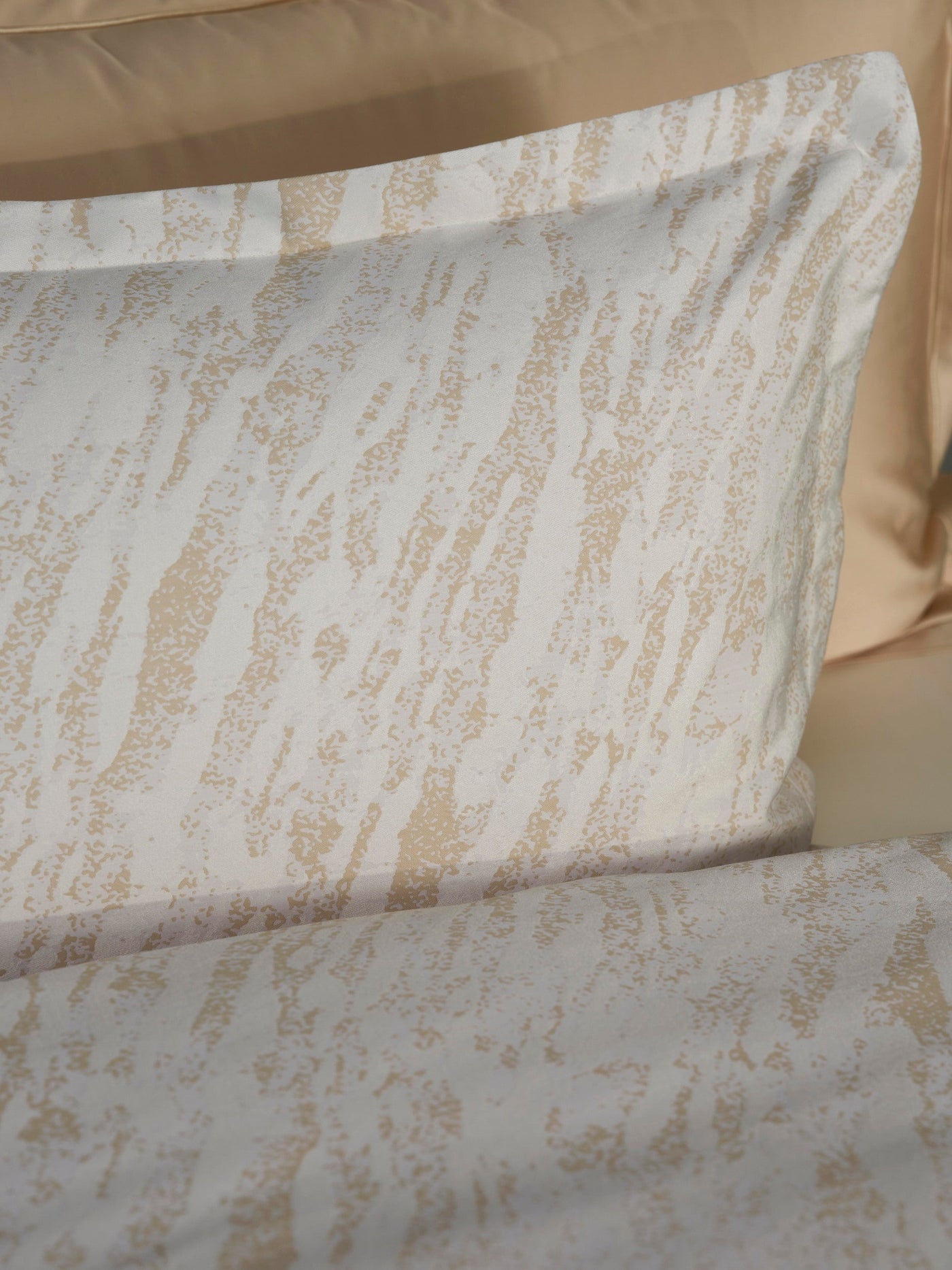 Close-up of Neve pillowcase showing ivory cotton with champagne abstract brushstroke pattern.