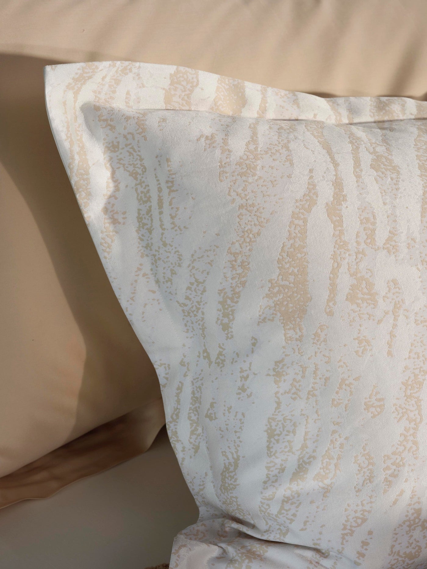 Close-up of Neve pillowcase corner showing champagne marble print on ivory cotton.