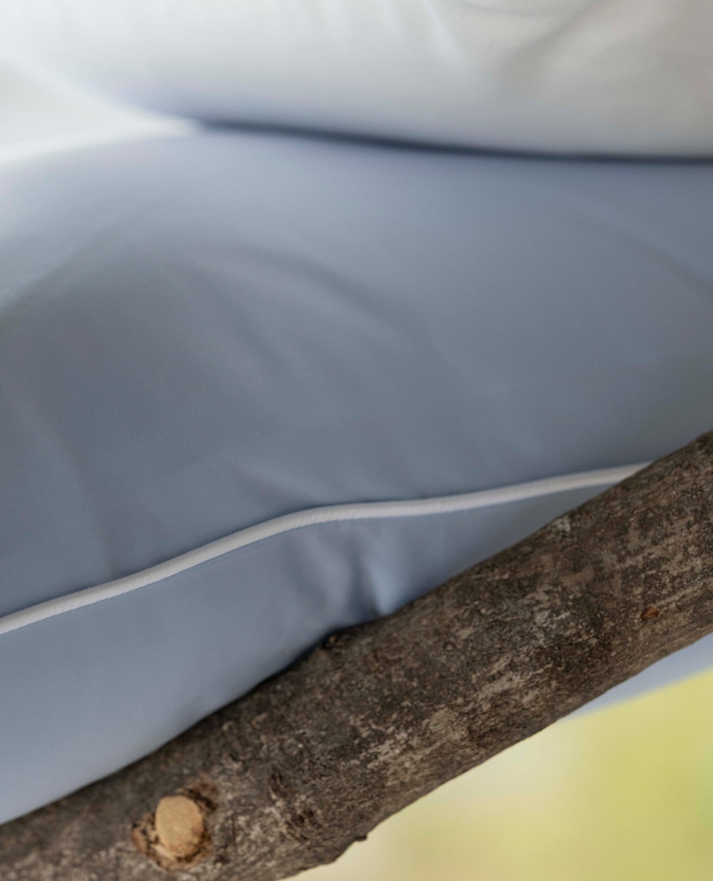 Light blue cover with white piping, draped over a natural wood branch. featuring Noa Pillow Cover by Celso de Lemos available at Linen Society.