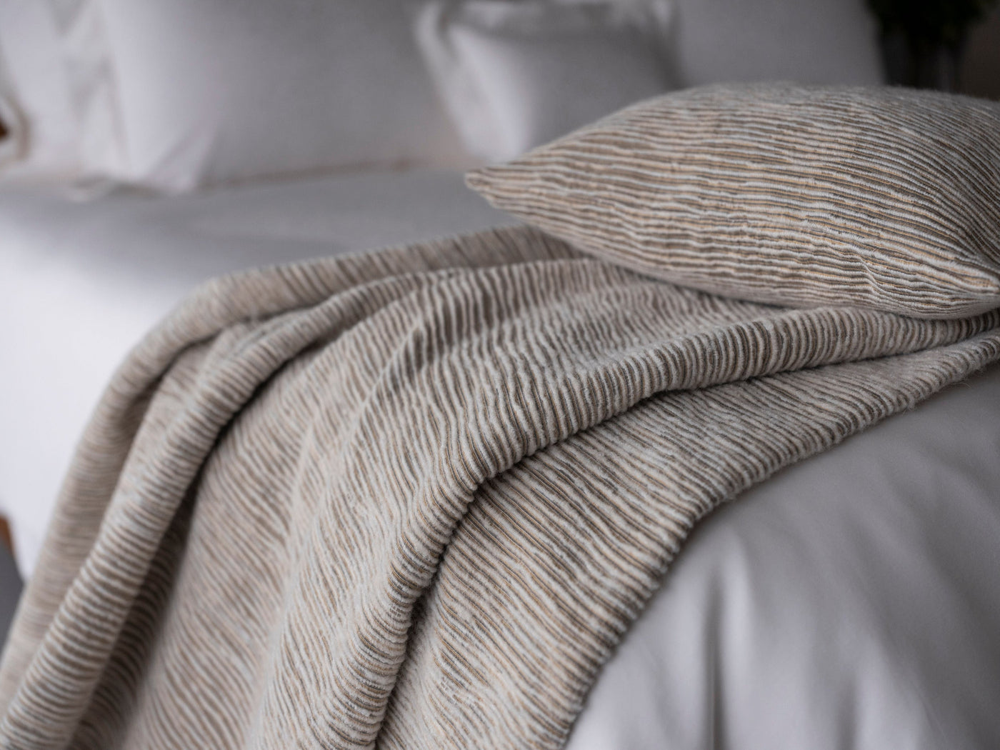 A textured, striped pillow cover rests on a bed with white linens. featuring Panama Pillow Cover by Celso de Lemos available at Linen Society.