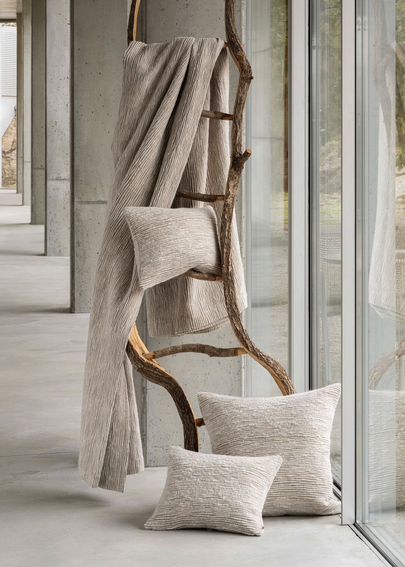 Textured natural linen pillow covers and throw are displayed on a rustic wooden ladder against a concrete backdrop, featuring Panama Pillow Cover by Celso de Lemos available at Linen Society.