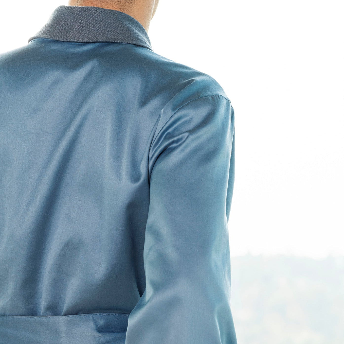 Person wearing a blue satin robe sitting on a stone ledge with a blurred natural background