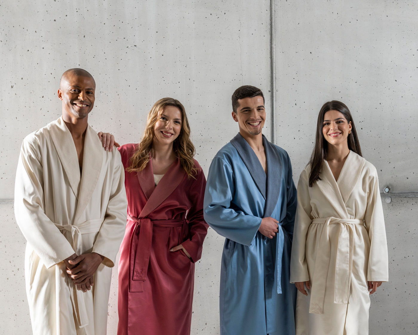 Four people wearing different colored robes standing against a plain wall.
