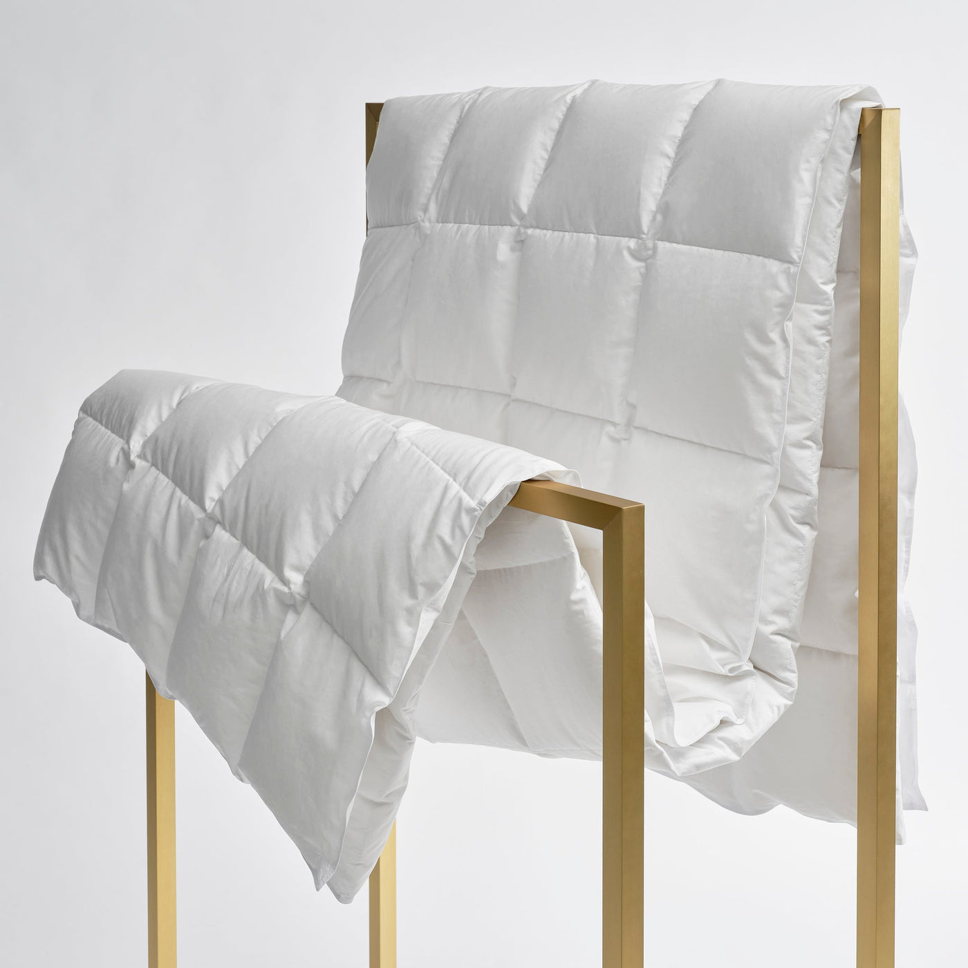 White comforter draped over a gold metal frame on a white background