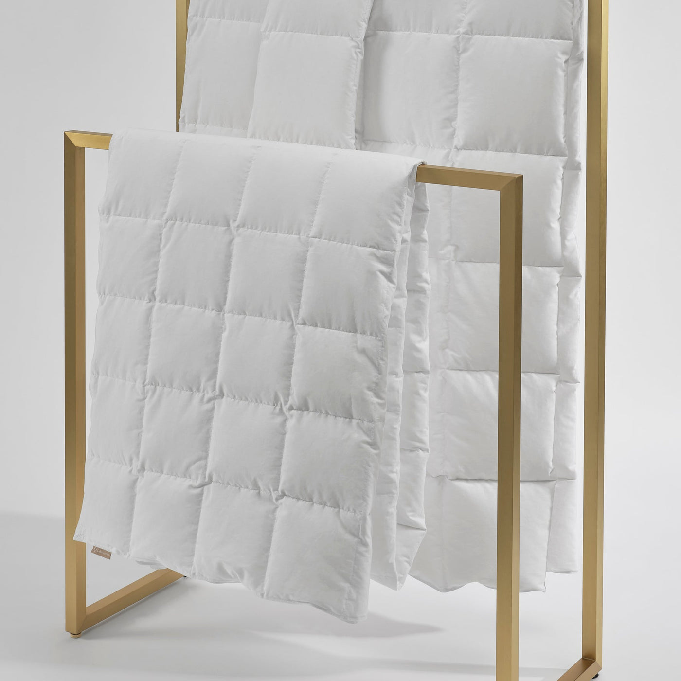 White quilted cover on a wooden rack against a light gray background