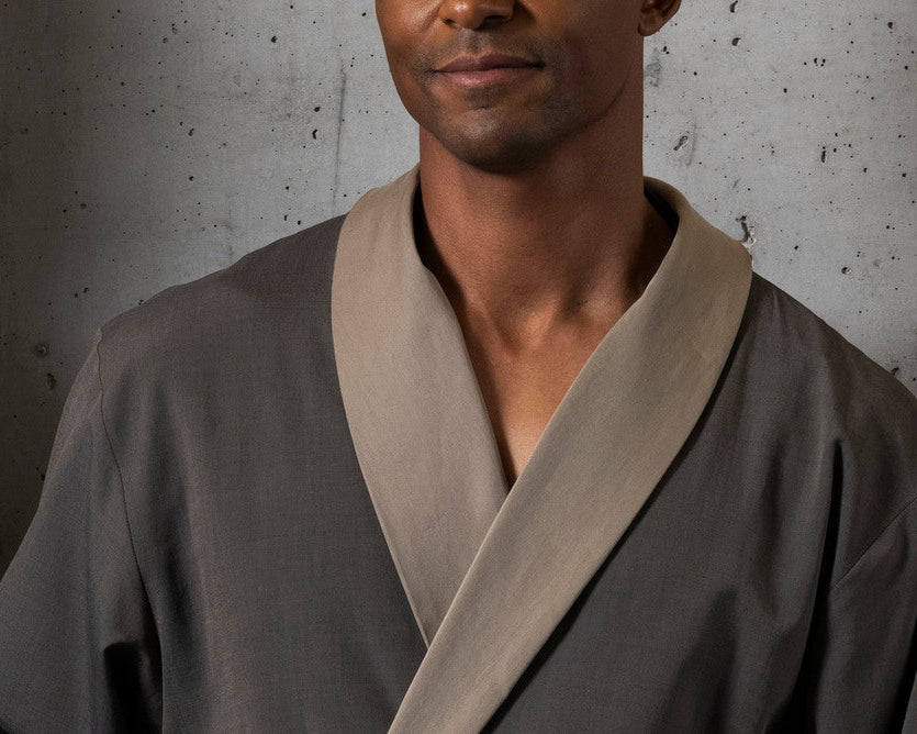 Two individuals wearing traditional robes against a concrete wall.