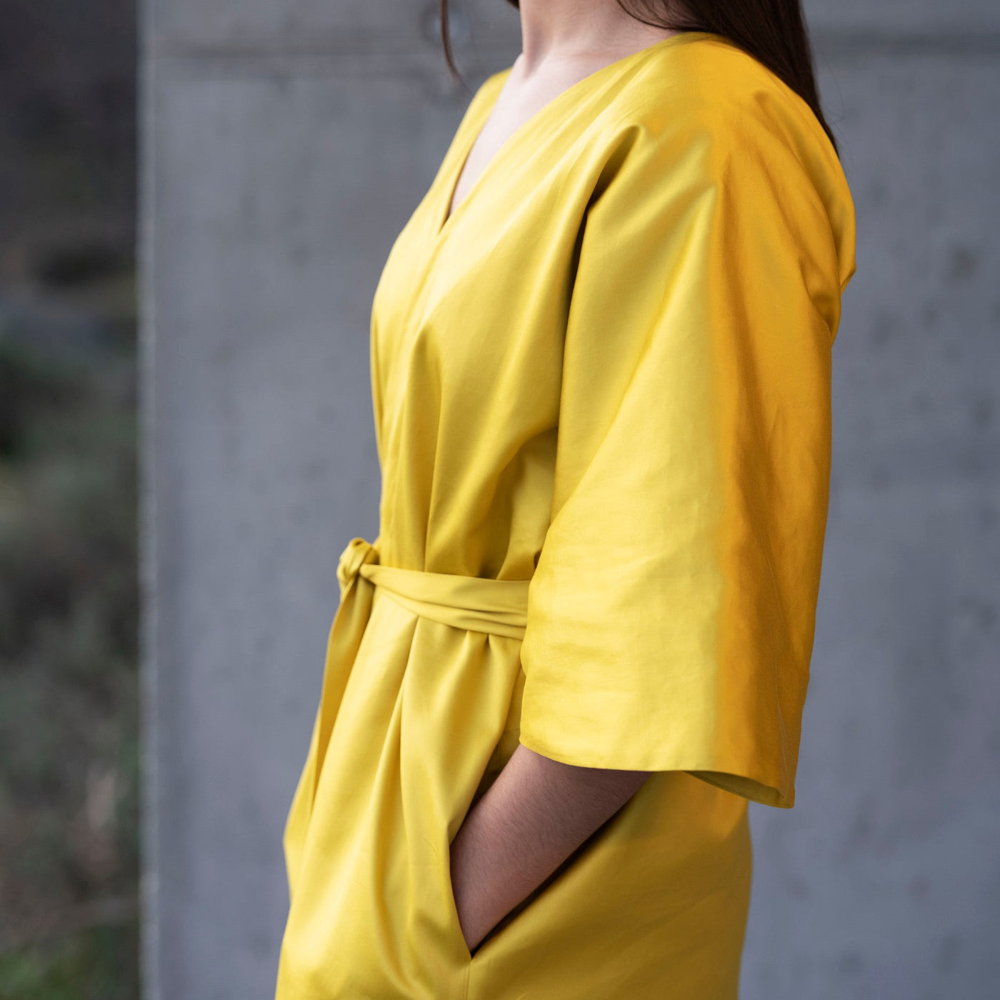 Woman wearing a yellow outfit standing against a concrete wall.
