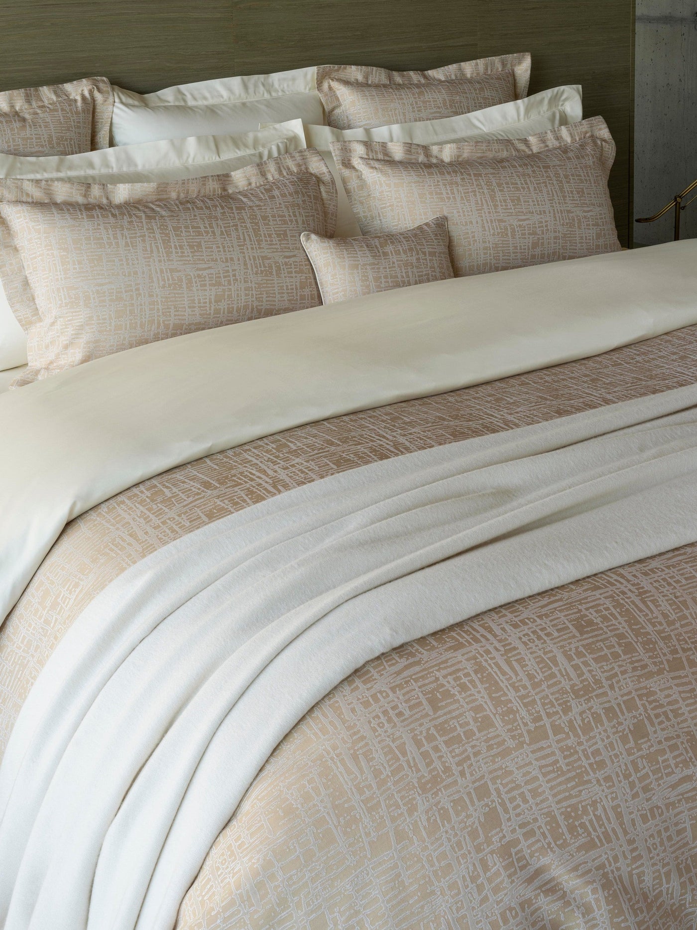Angled view of champagne textured duvet cover with ivory throw layered across a styled bed.