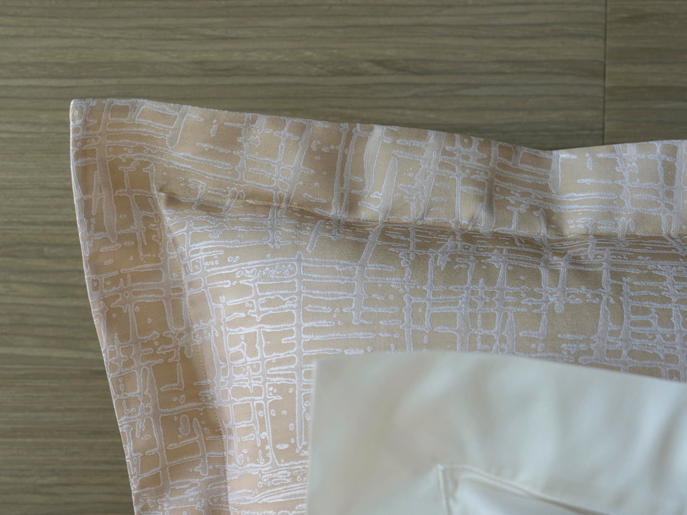Close-up of Celso de Lemos Partition pillowcase corner, champagne geometric print with white hem detail.