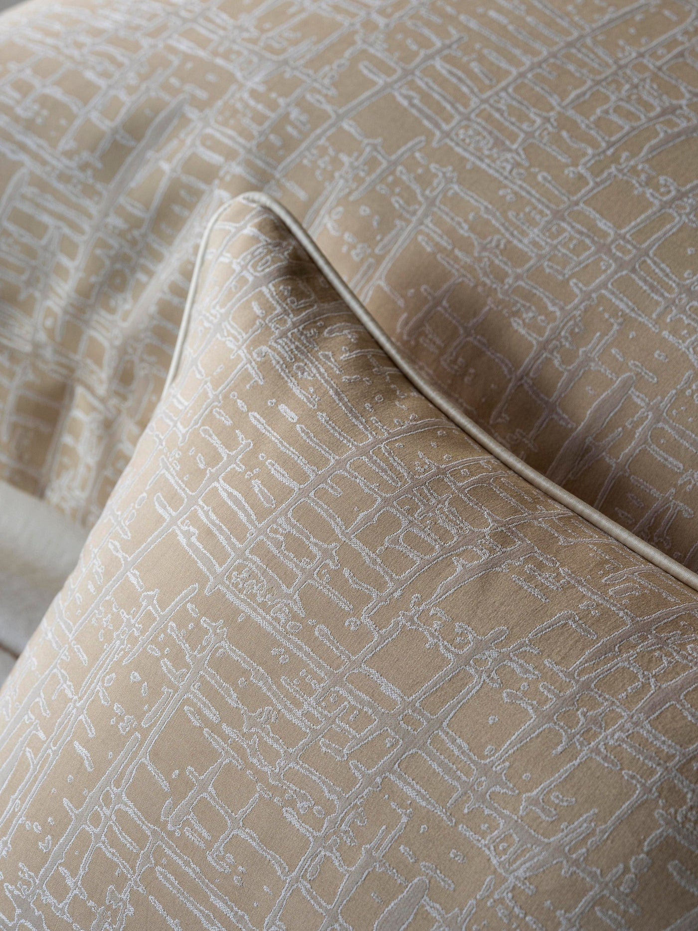 Close-up of champagne pillowcase with ivory geometric grid pattern and contrast piped edge.