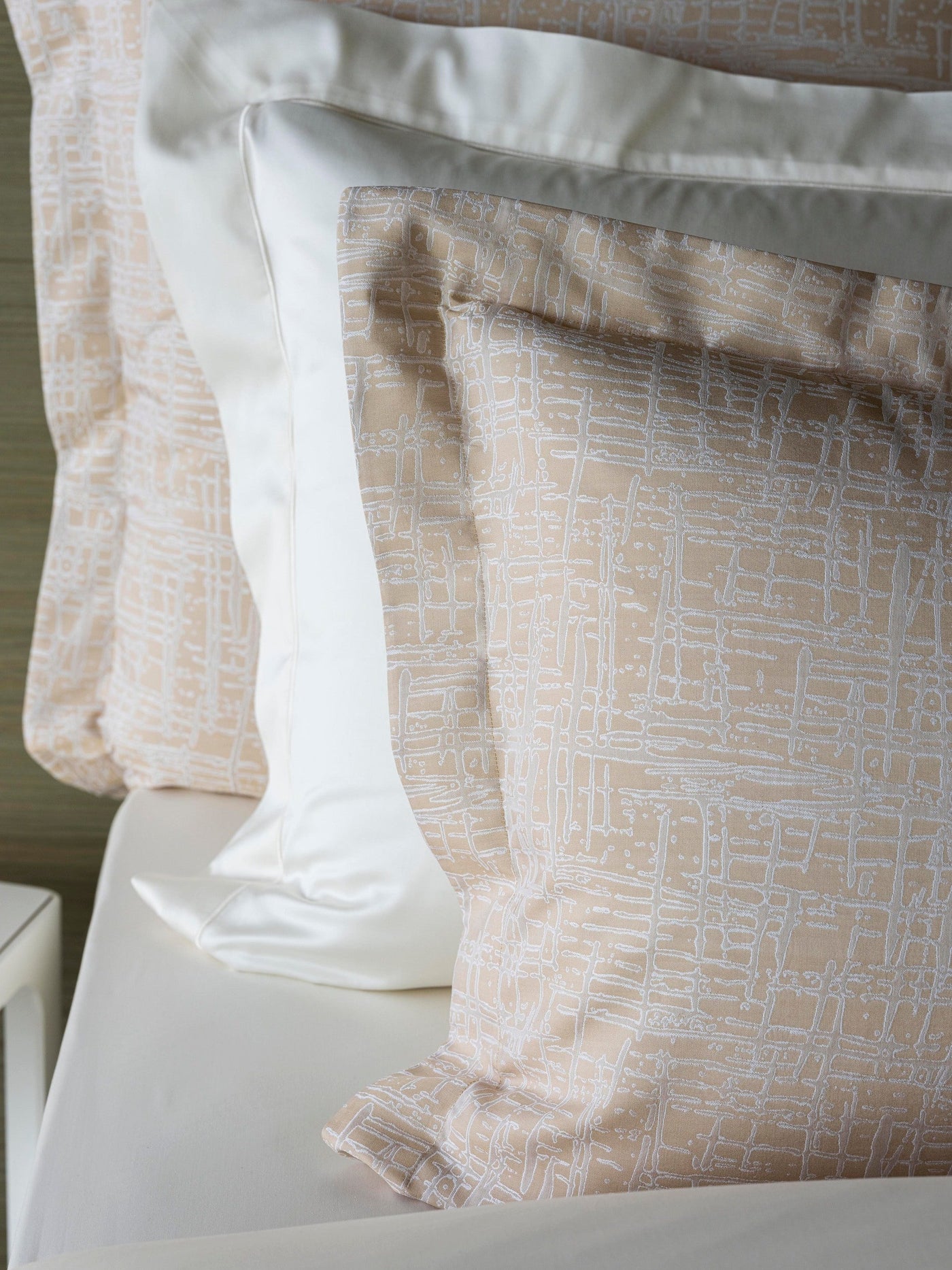Close-up of Celso de Lemos Partition pillowcase in sand, white geometric line pattern, flanked by white pillows.