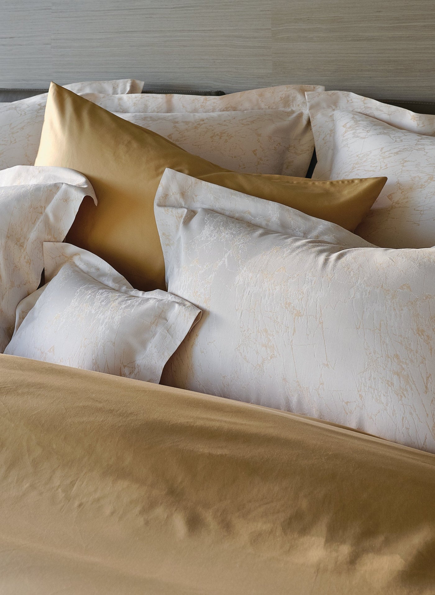 Ivory jacquard pillowcases with gold botanical pattern styled alongside champagne satin pillows.