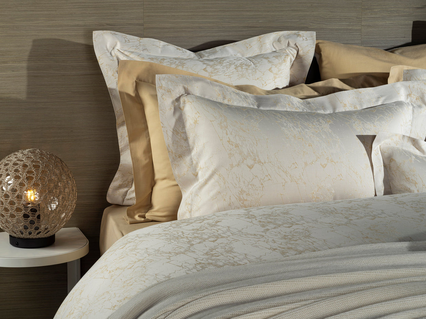 Ivory jacquard pillowcase with floral pattern, styled with champagne and gold bedding layers.