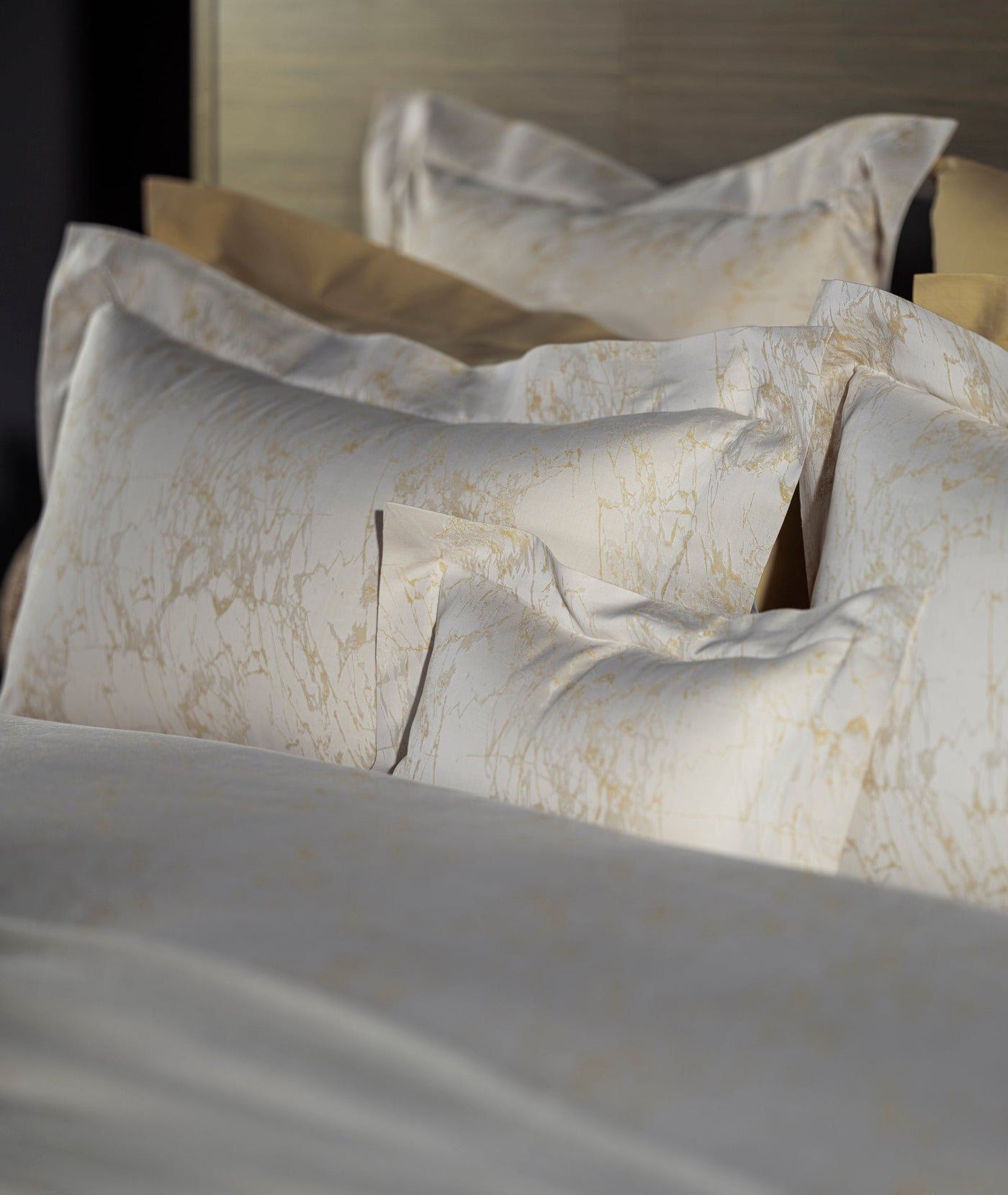Ivory and gold marble-jacquard pillowcases stacked on a styled bed, flange detail visible.